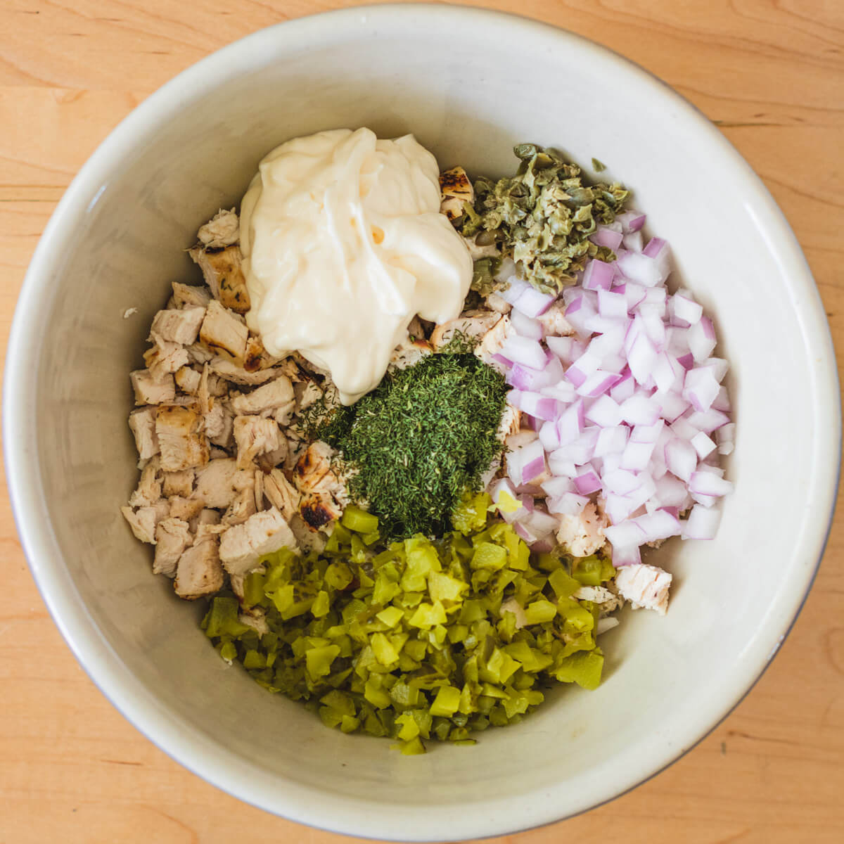 A bowl containing all of the ingredients for Dill Pickle Chicken Egg Salad before they are mixed together.