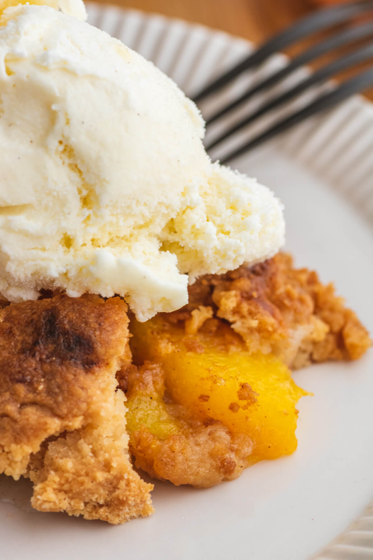 A white plate containing a scoop of peach cobbler dump cake topped with a scoop of ice cream.