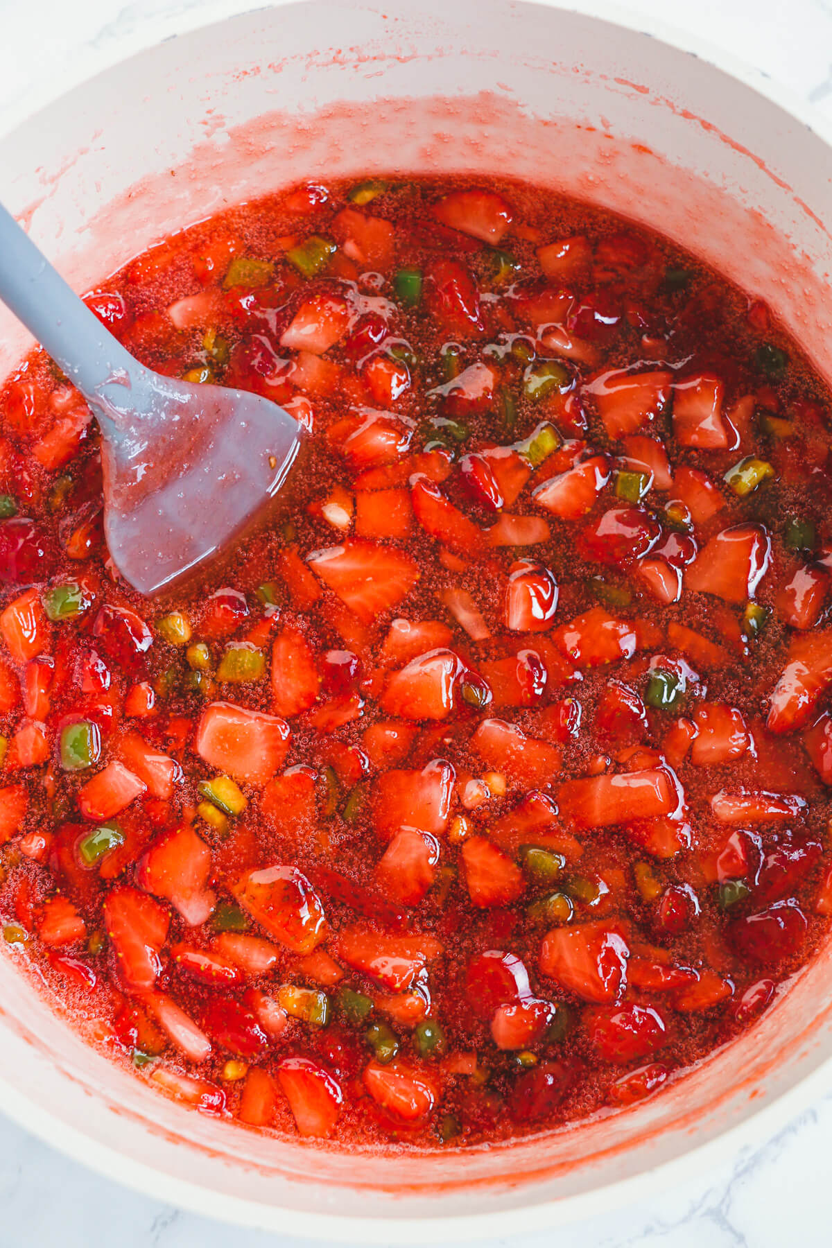 A large Dutch oven filled with mashed and cooked diced strawberries and jalapeños.