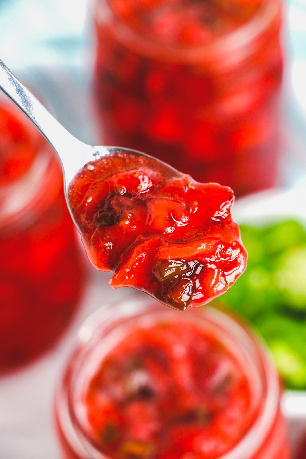 A silver spoon containing Strawberry Jalapeño jam over an open jar of the same jam.