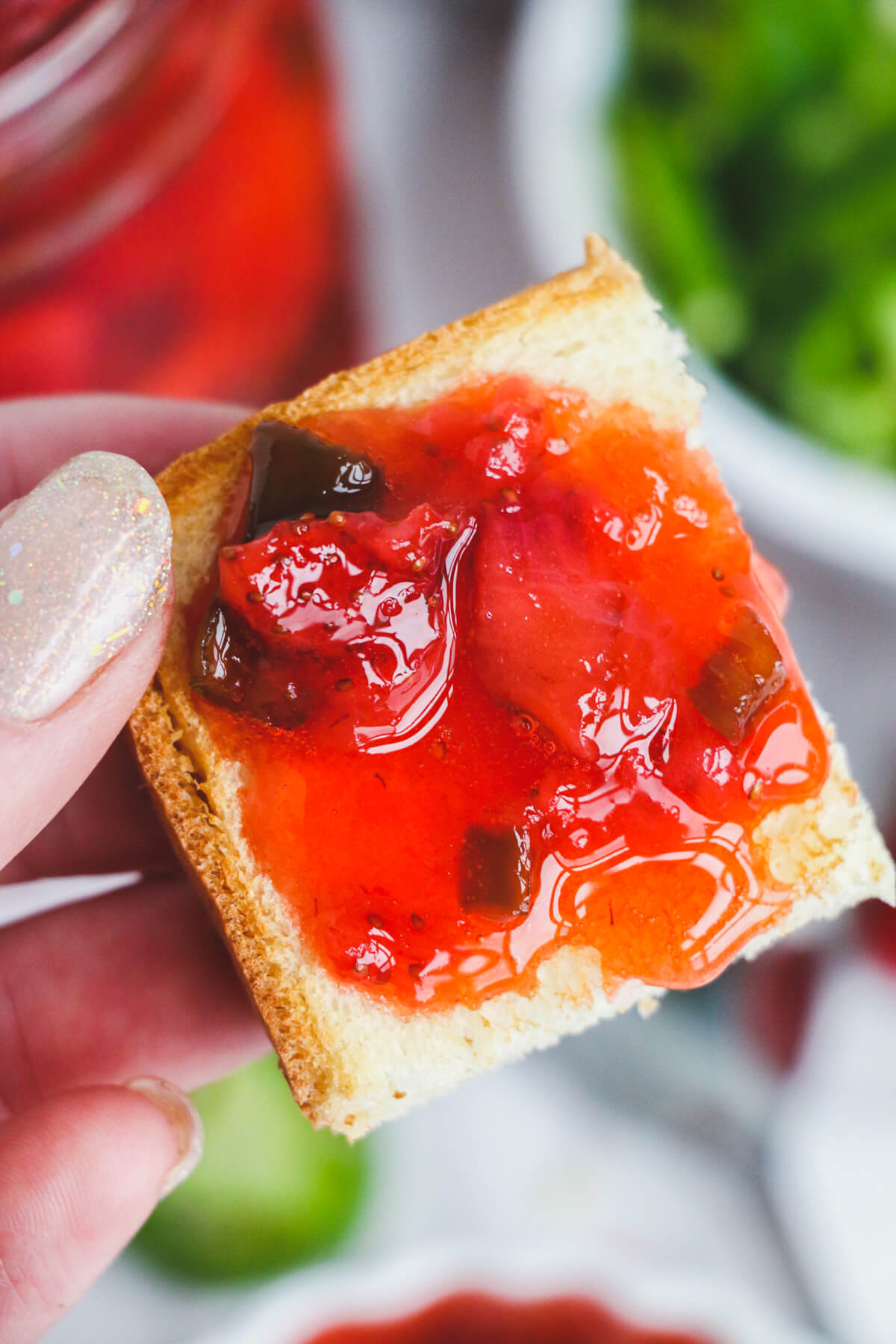 A hand holds a piece of toast slathered with chunky Strawberry Jalapeño jam.