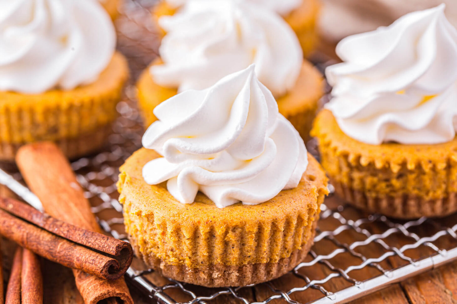 A wire baking rack containing four mini pumpkin cheesecakes topped with whipped cream.