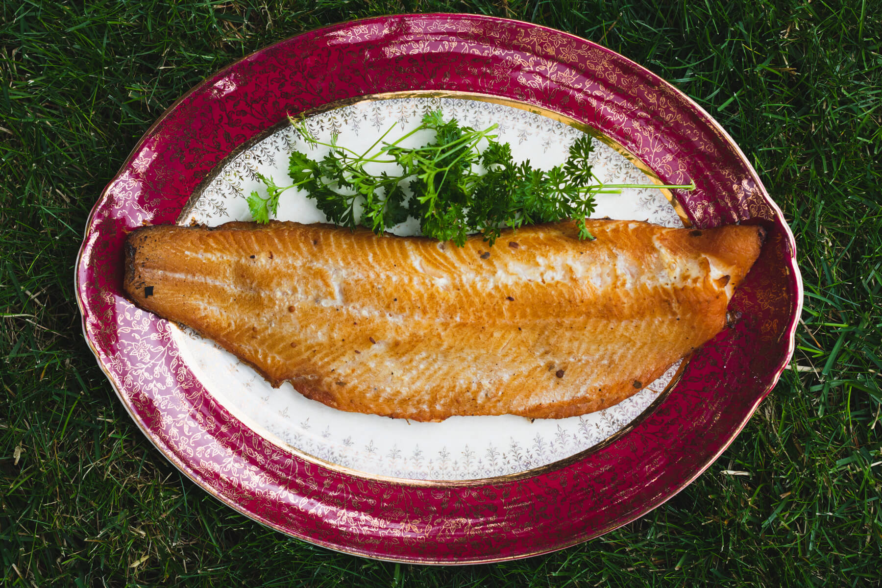 A vintage platter containing one filet of smoked trout garnished with fresh parsley.