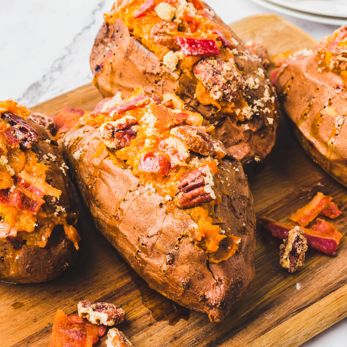 Four Twice Baked Sweet Potatoes topped with crispy bacon and pecans on a wooden serving board.