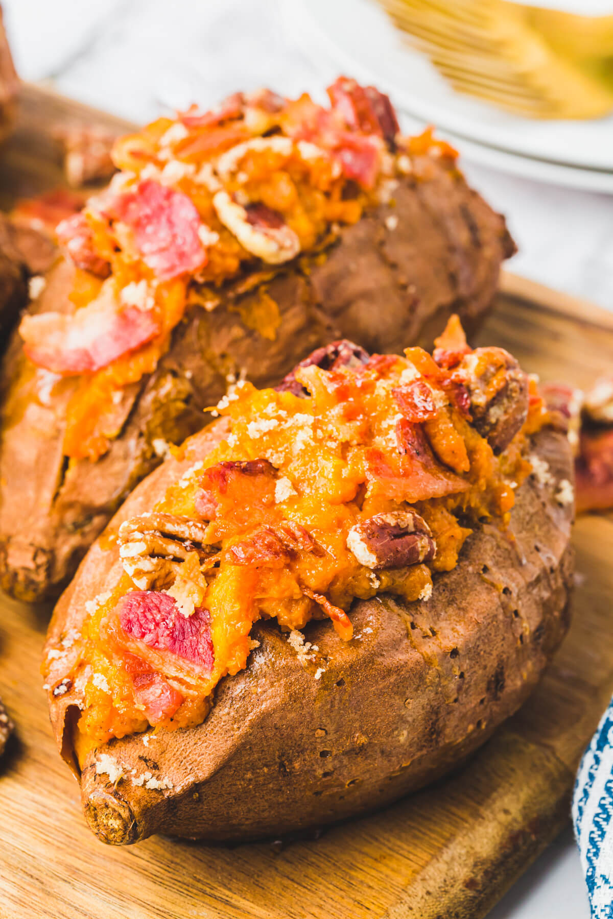 Two Twice Baked Sweet Potatoes topped with crispy bacon and pecans on a wooden serving board.