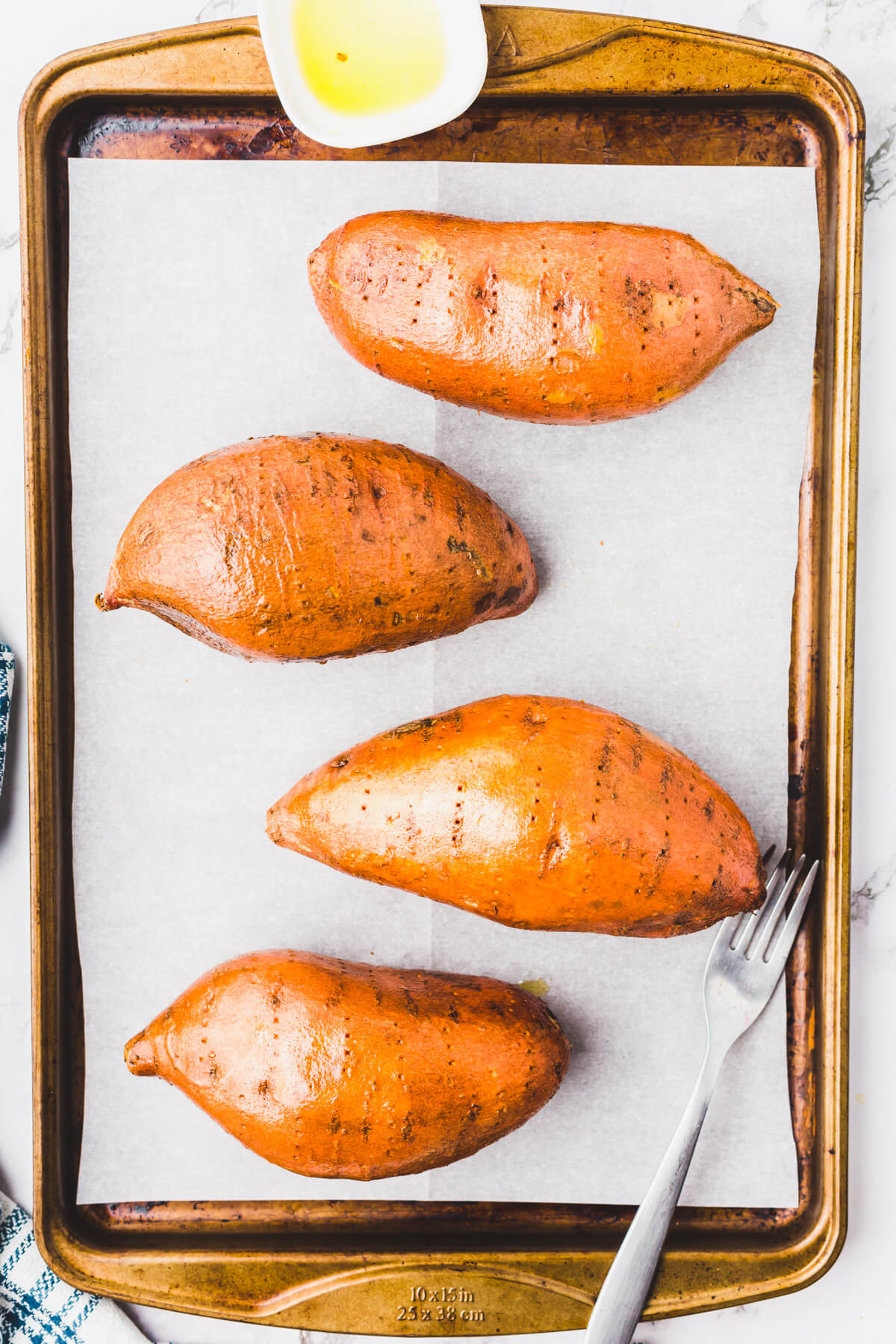 Four sweet potatoes on a parchment lined baking sheet.
