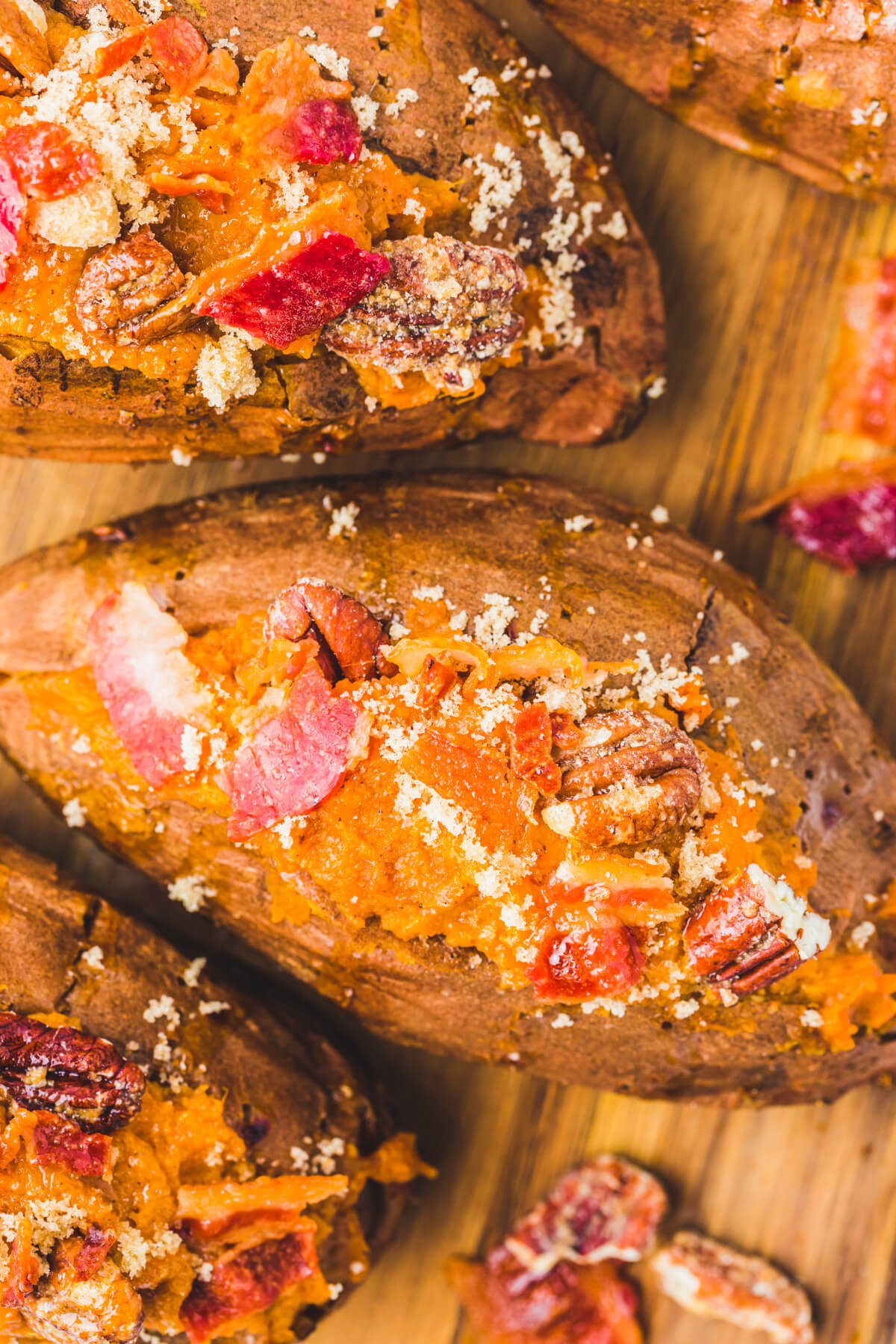 Three Twice Baked Sweet Potatoes topped with crispy bacon and pecans on a wooden serving board.