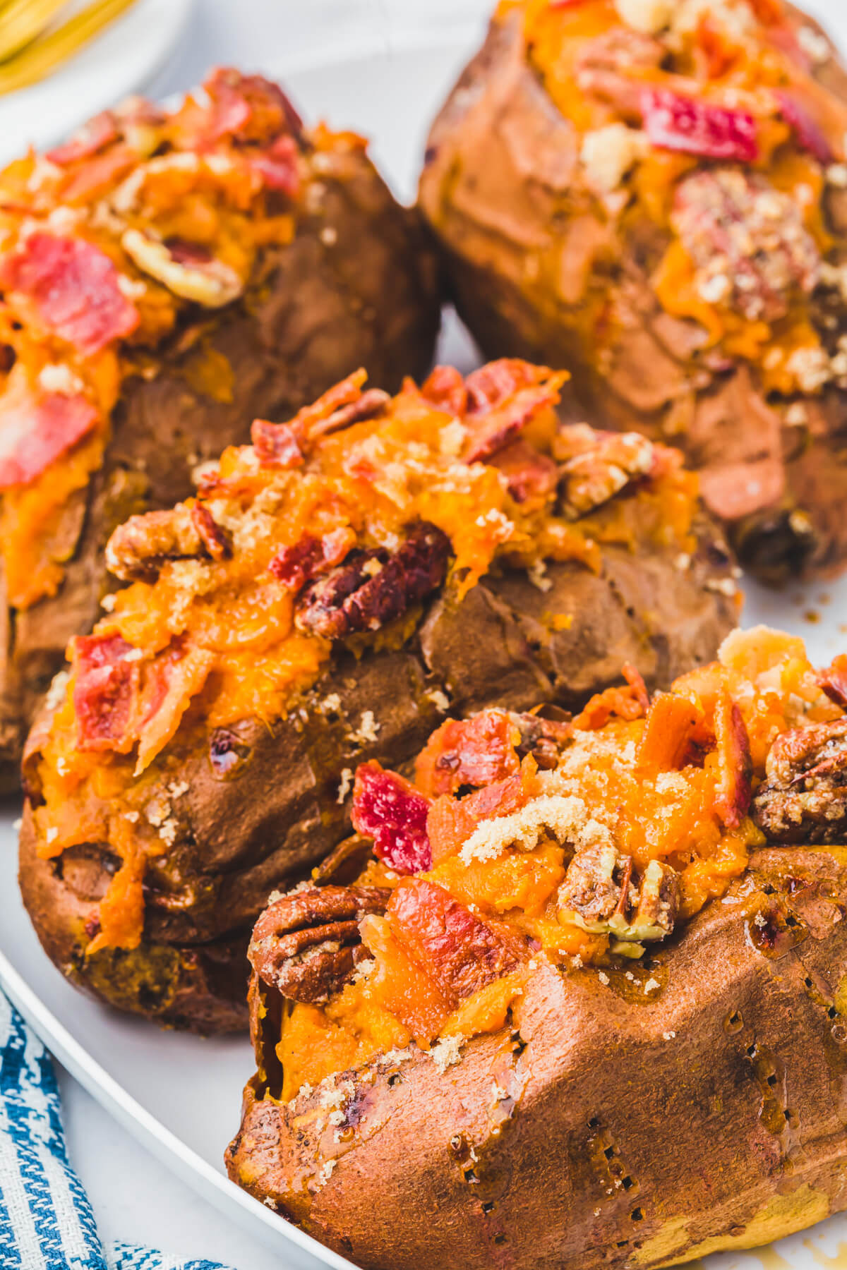 Four Twice Baked Sweet Potatoes topped with crispy bacon and pecans on a white plate.