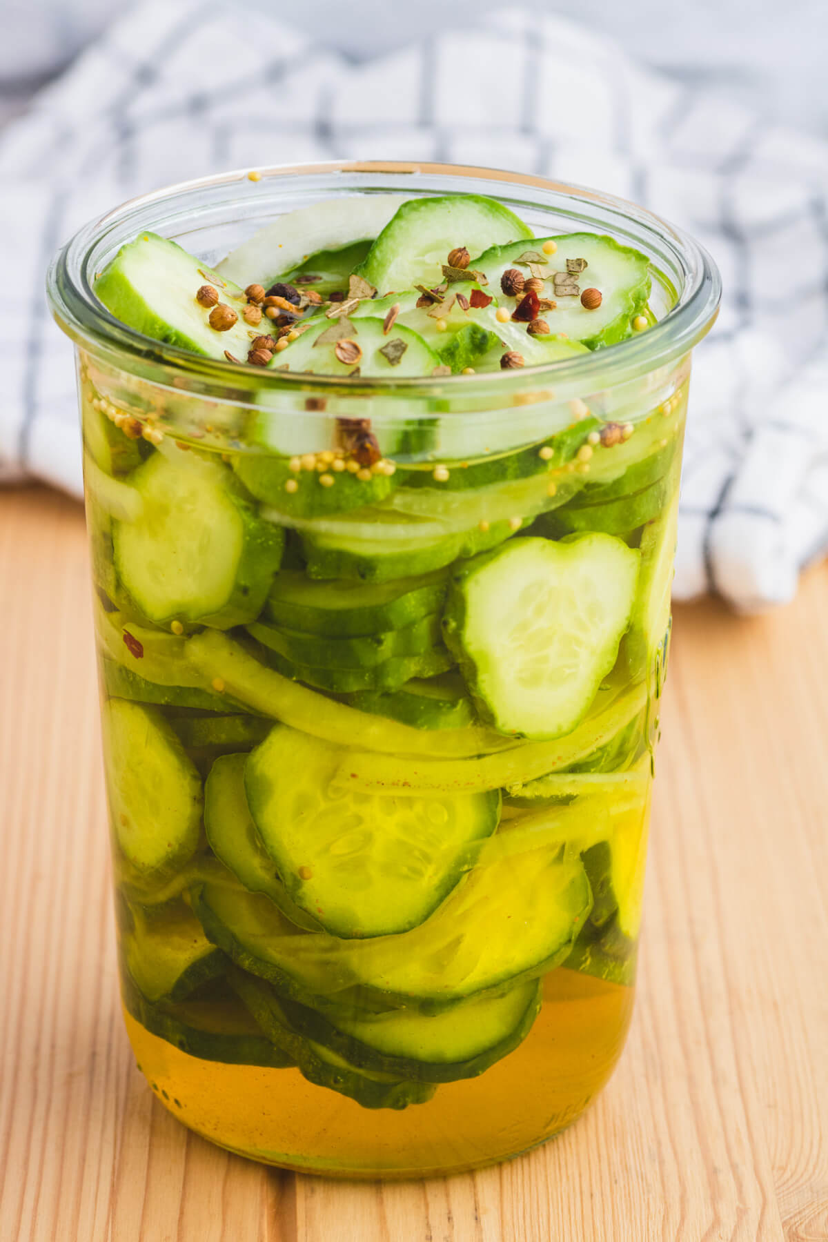 A glass jar filled with sliced cucumbers, onions, brine, and pickling spices about to be Refrigerator Bread and Butter pickles.