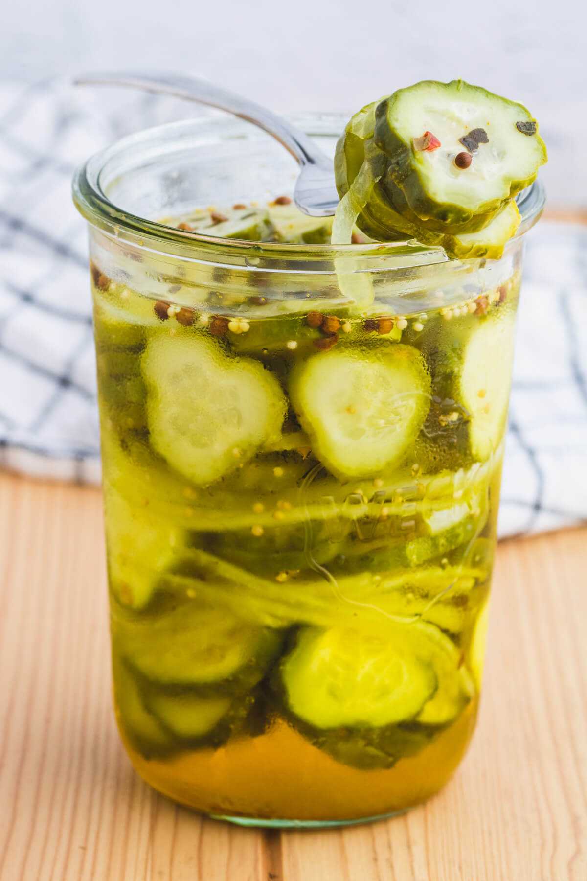 A fork holding sliced Refrigerator Bread and Butter pickles over a glass jar of pickles.