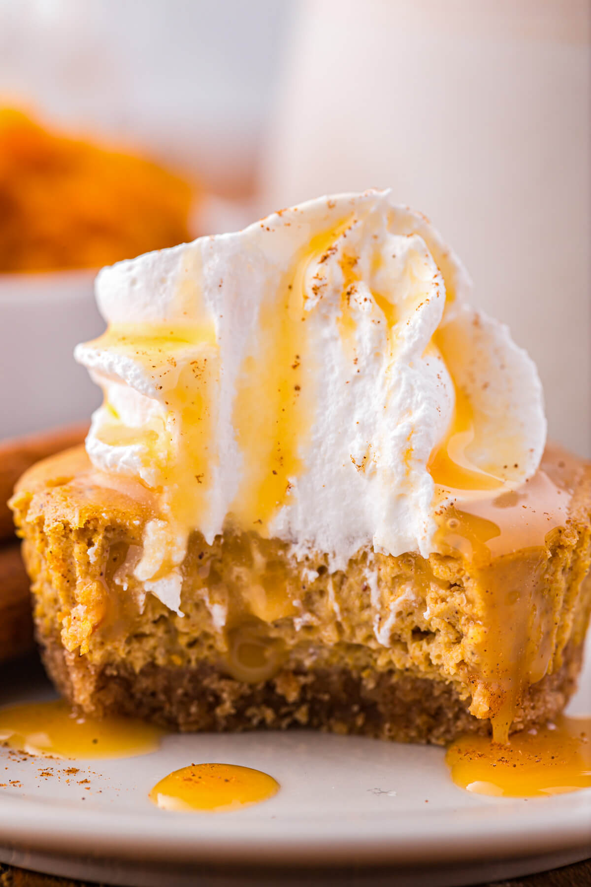 A whipped cream topped mini pumpkin cheesecake with a bite taken out and dripping with caramel sauce.