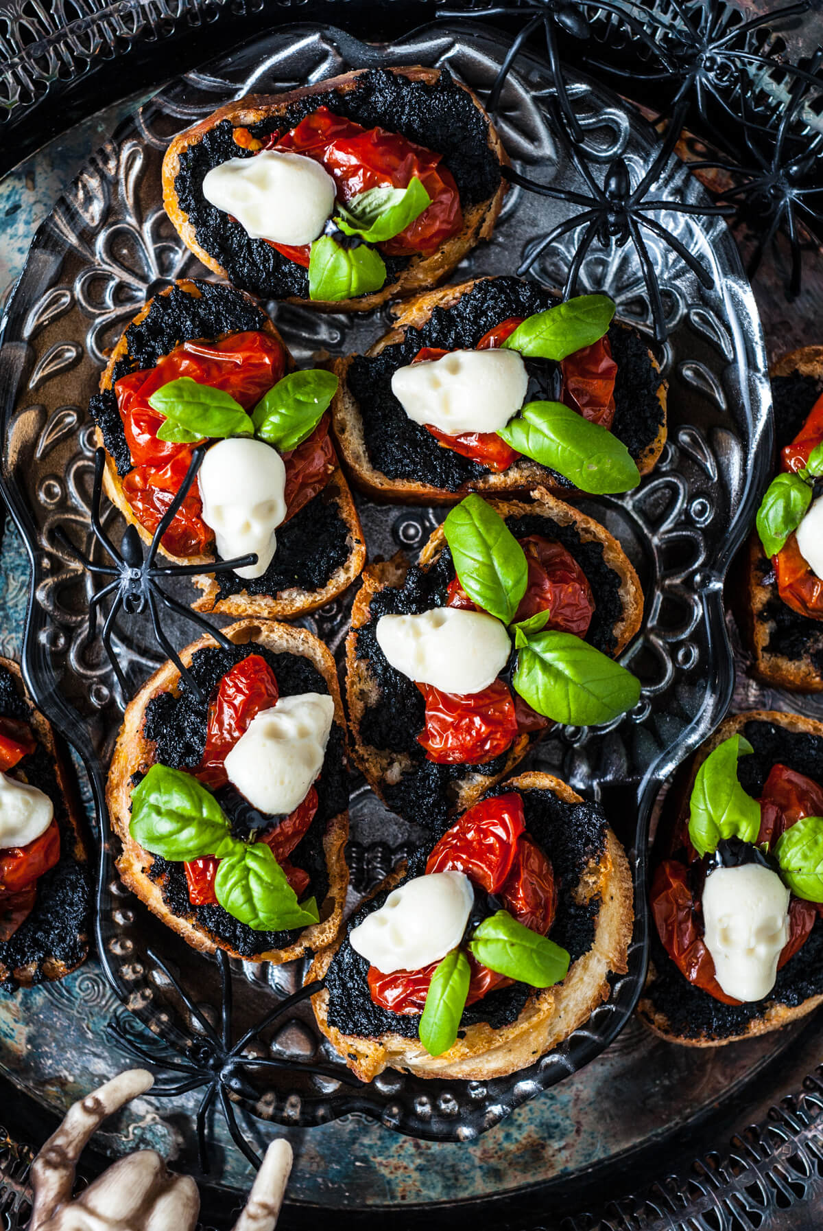 A spooky scene featuring a silver tray of caprese crostini decorated with mozzarella skulls and spiders.