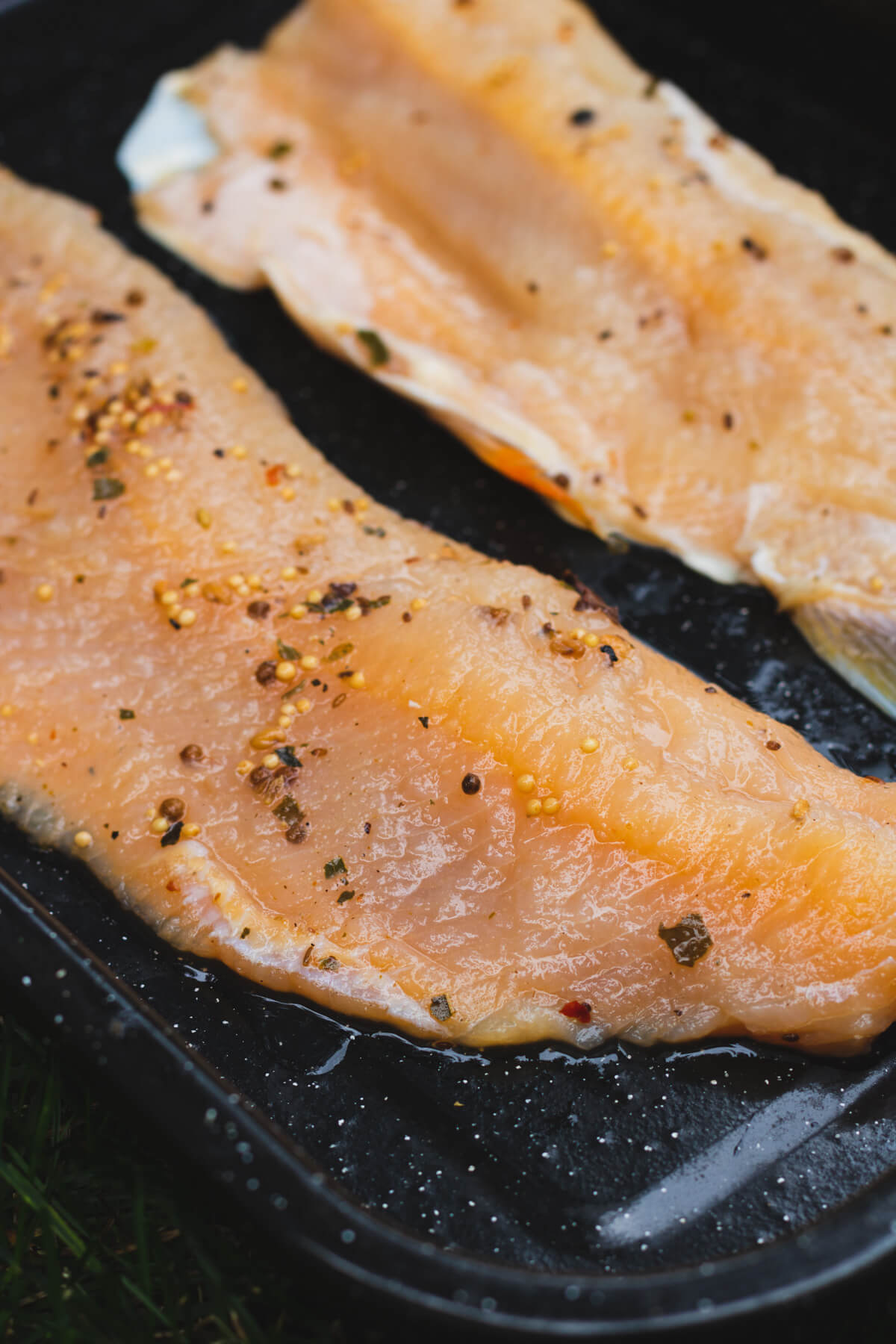 A black enamel tray containing two brined trout filets ready for the smoker.