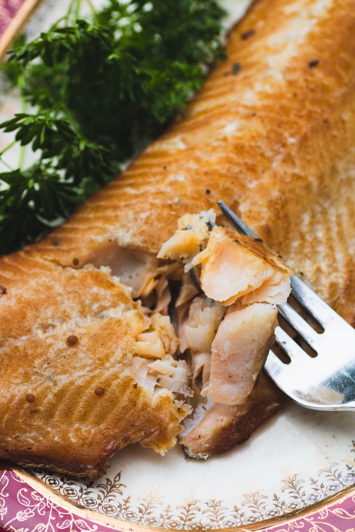 A fork holding a bite of juicy smoked trout above a whole trout filet.