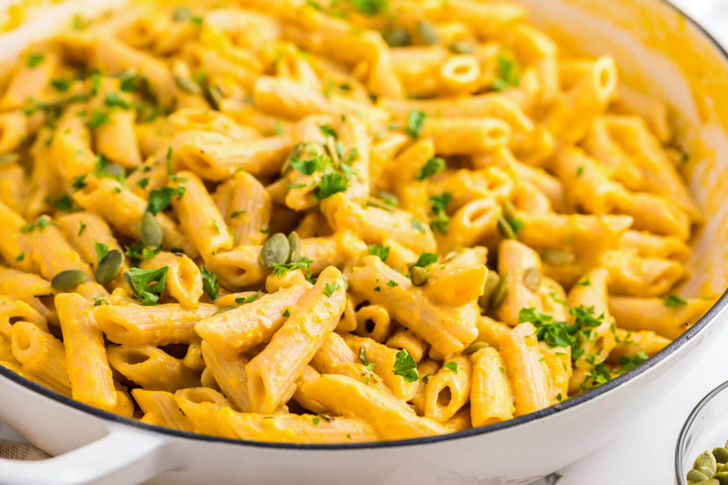 A white enameled pan filled with penne in a creamy pumpkin pasta sauce.