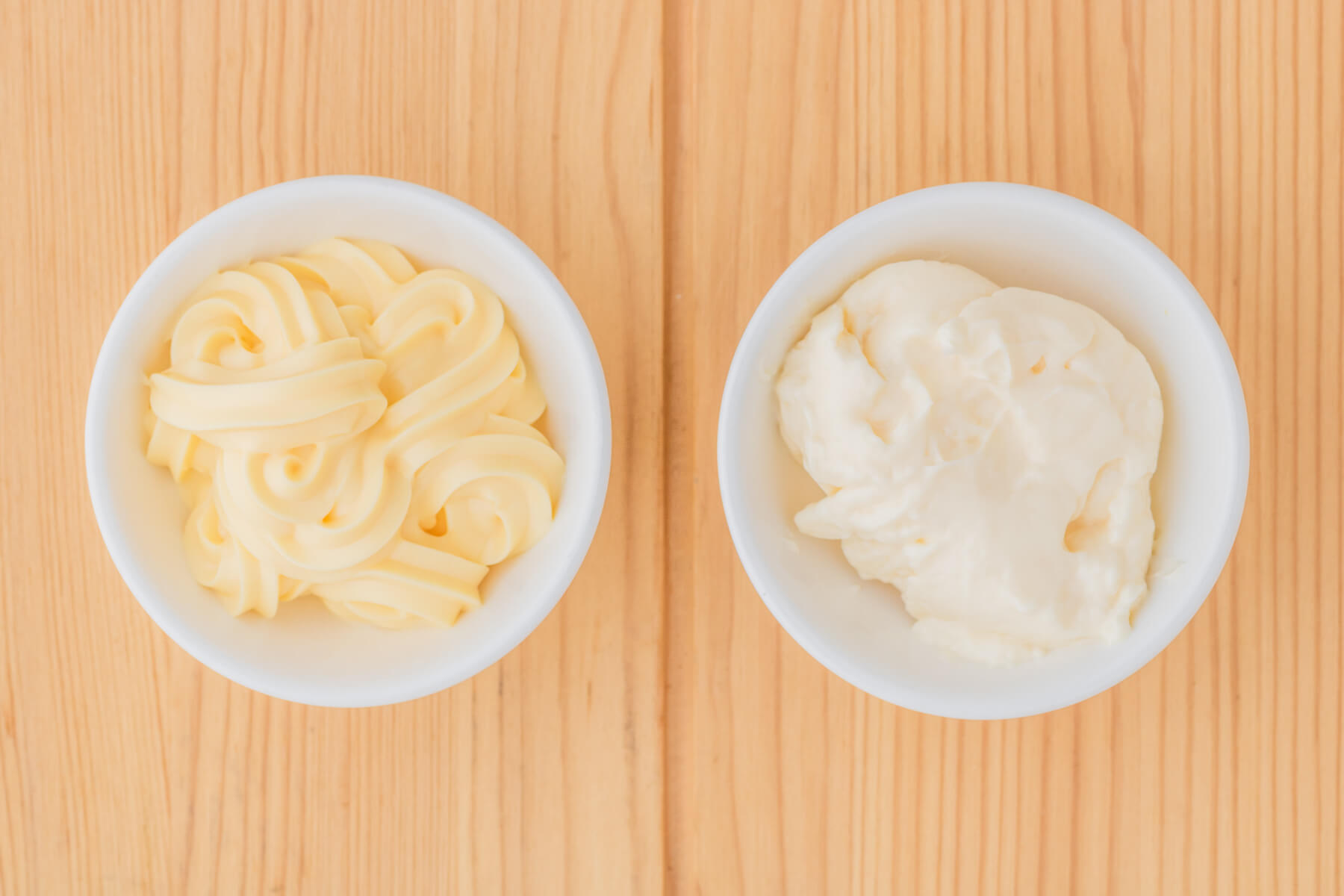 Two white bowls filled mayonnaise showing the difference in colour and texture between Kewpie Mayonnaise and Hellman's Mayonnaise.