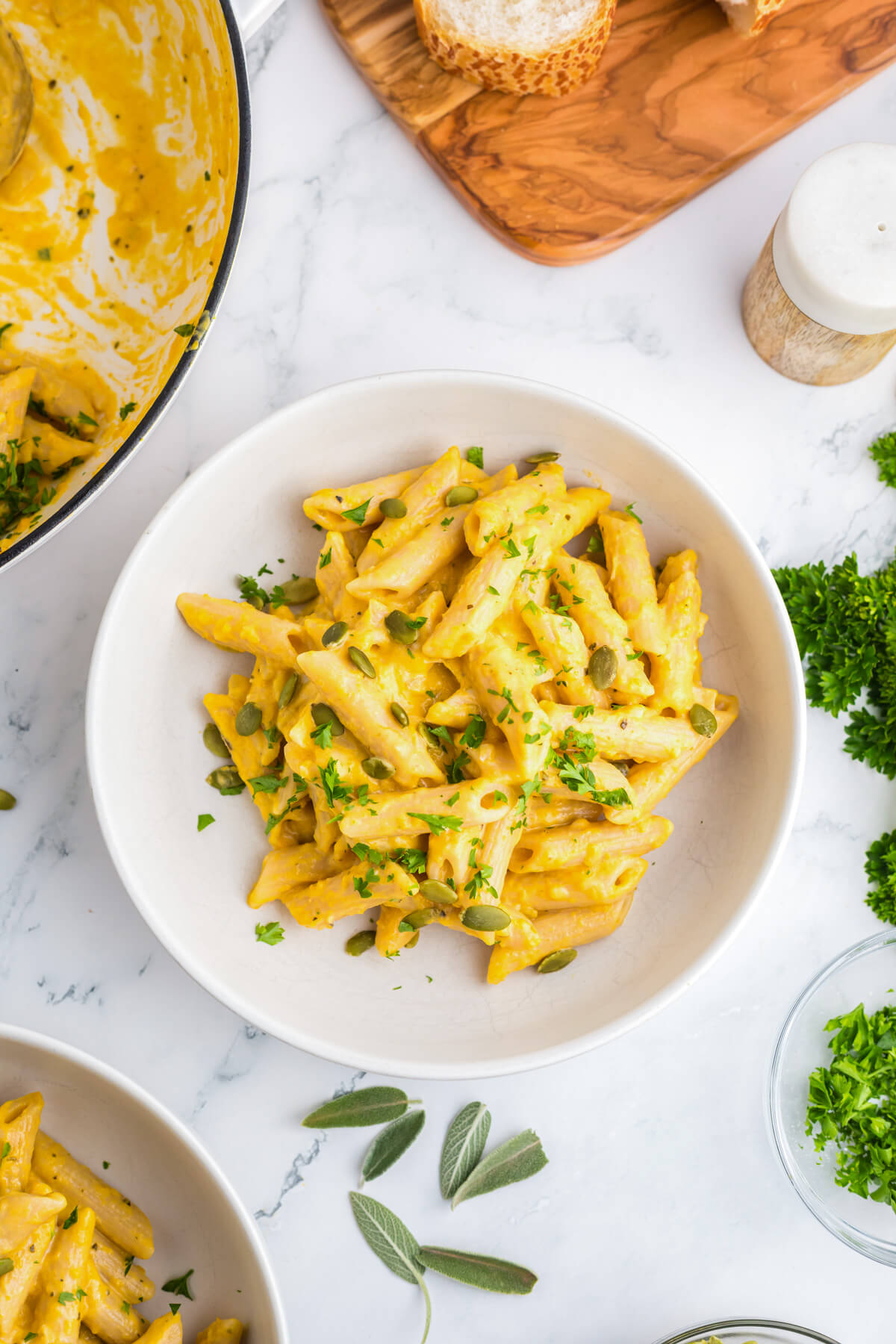 A white bowl containing creamy penne in a pumpkin pasta sauce garnished with pepitas and parsley.