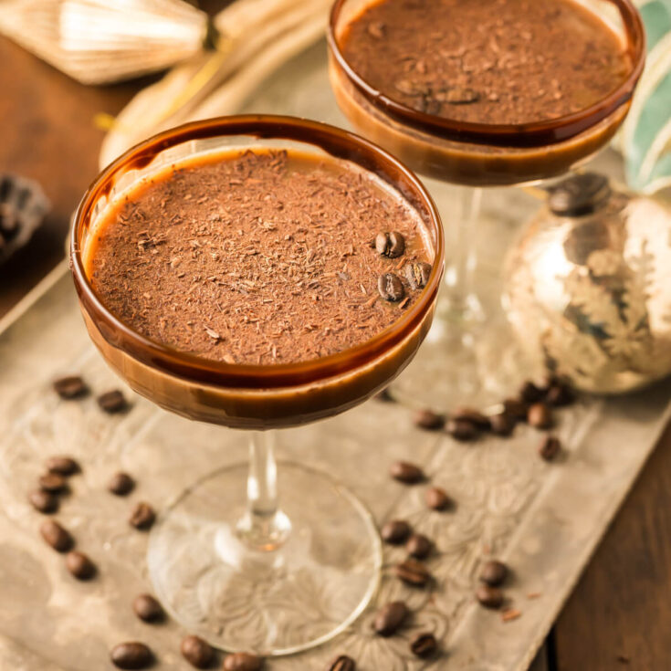 Two creamy brown Chocolate Espresso Martinis in coupe cocktail glasses garnished with chocolate rim and chocolate shavings.