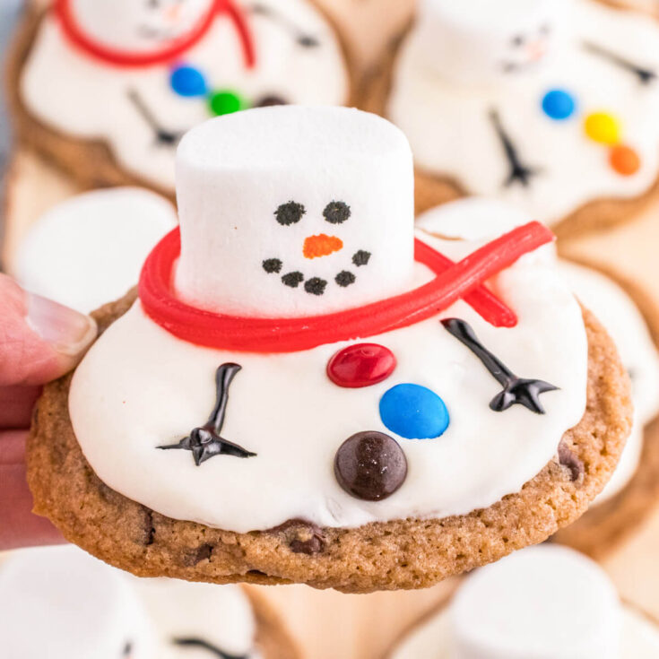 A group of Melted Snowman Cookies featuring white frosting on a chocolate chip cookie decorated with a marshmallow snowman.