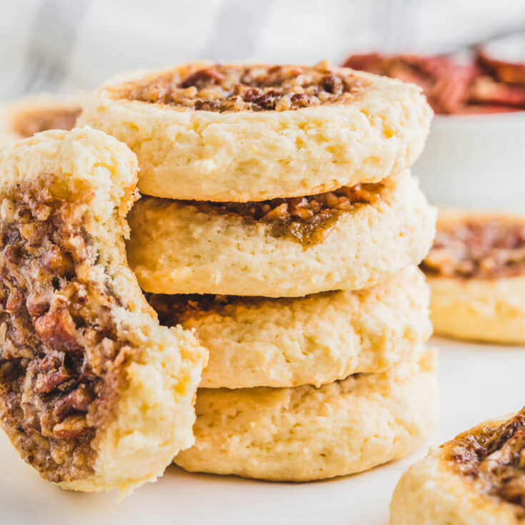 A stack of four pecan pie cookies beside a cookie with a bite missing.