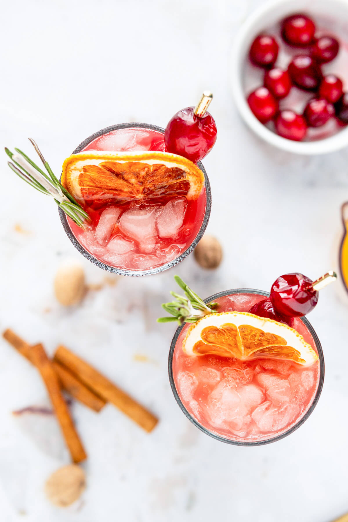 An overhead photo of the tops of two icy mulled cranberry madras cocktails garnished with dried orange wheels, cranberries, and sprigs of rosemary.