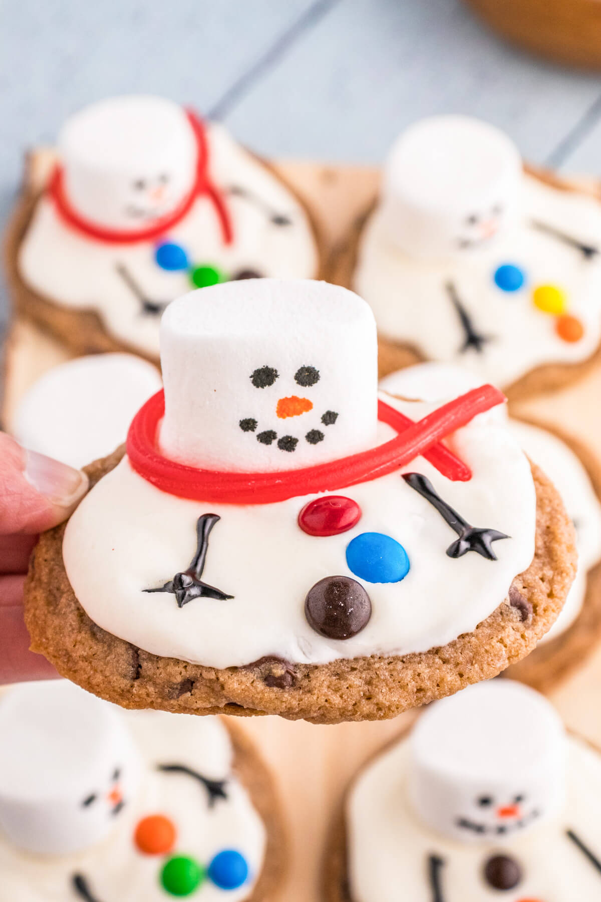 A group of Melted Snowman Cookies featuring white frosting on a chocolate chip cookie decorated with a marshmallow snowman.