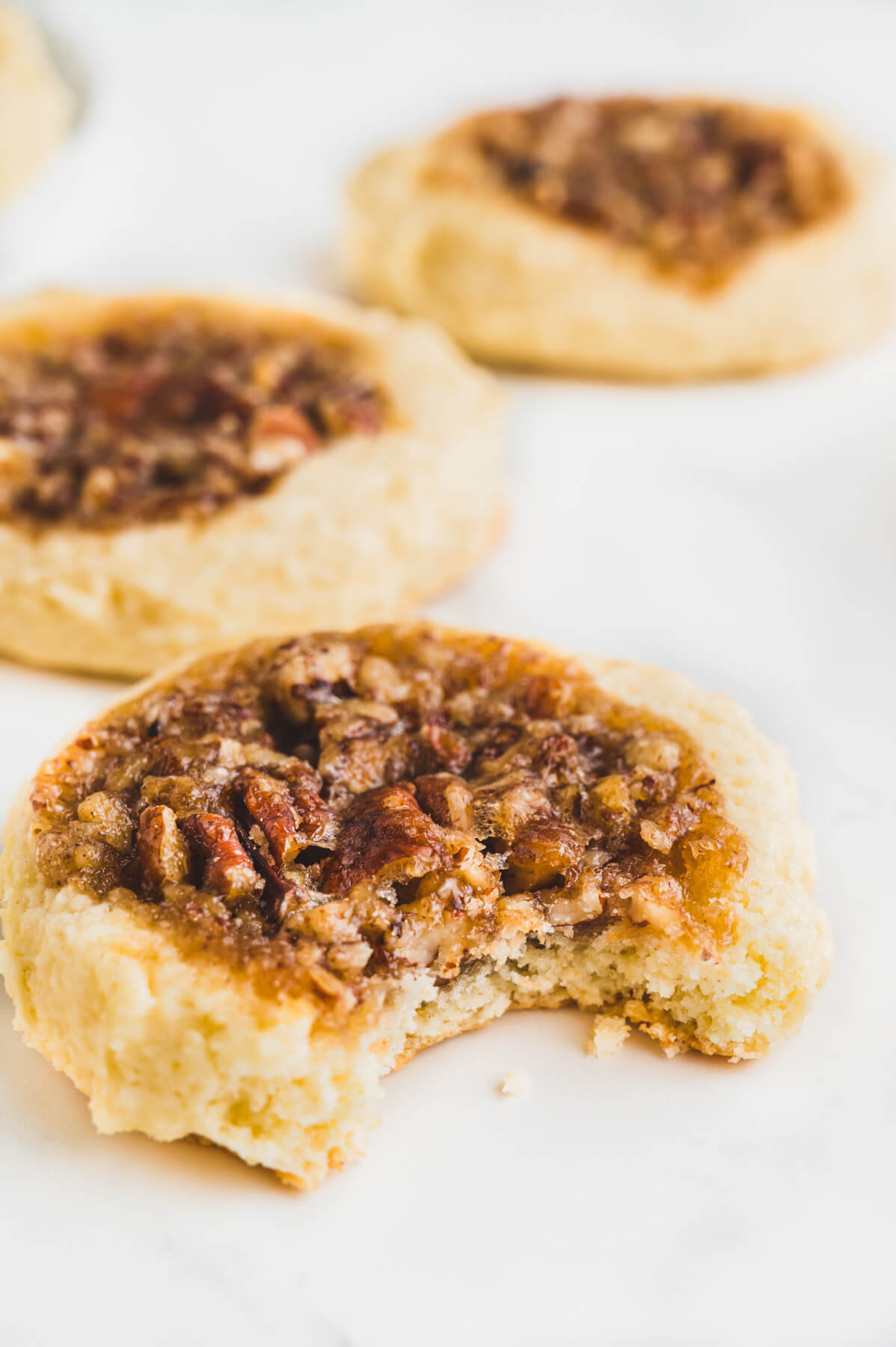 Three pecan pie cookies on a white background with a bite missing out of the closest cookie.