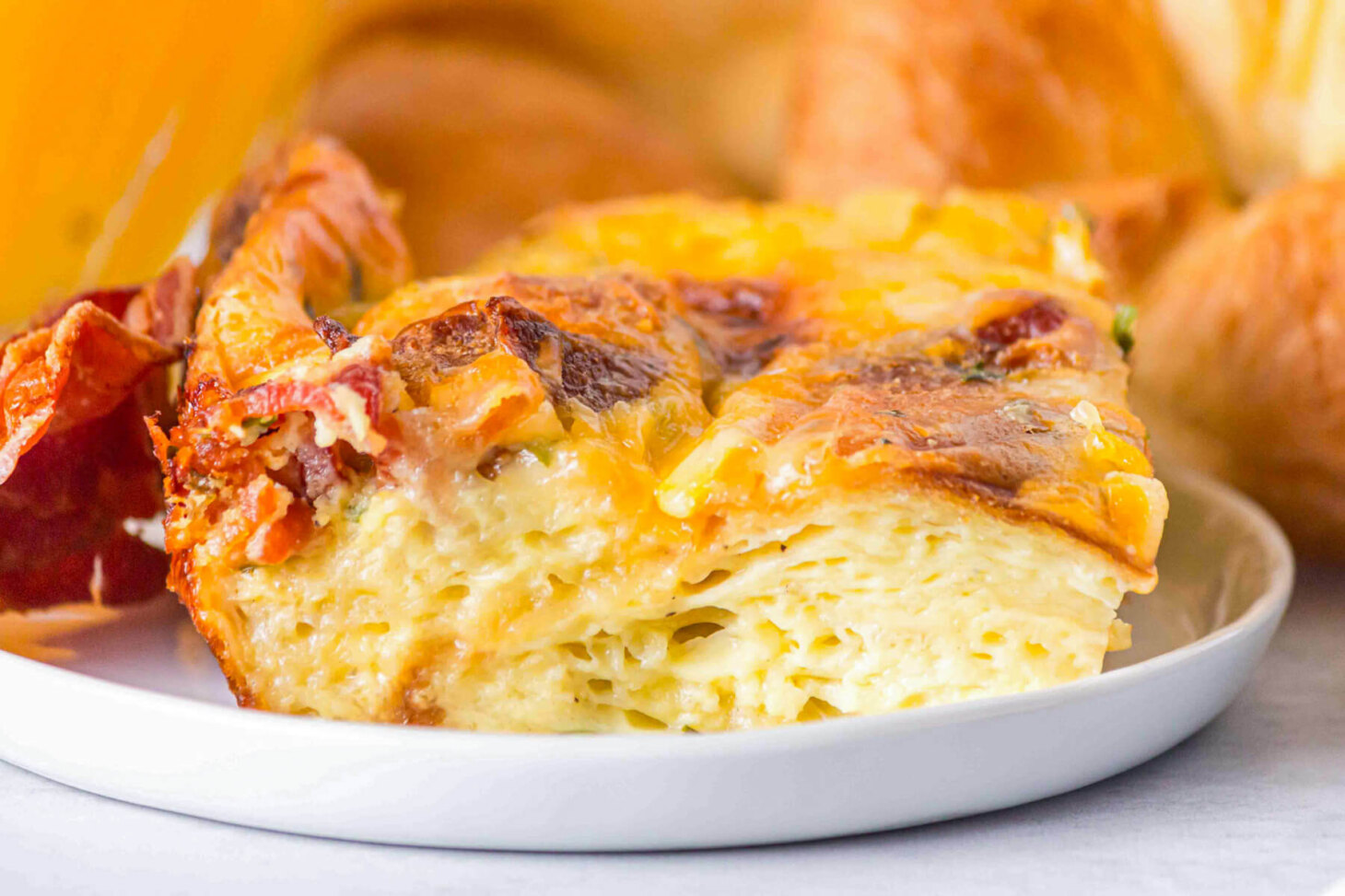A square serving of Croissant breakfast casserole showing the layers of eggs, croissants, bacon, and cheese.