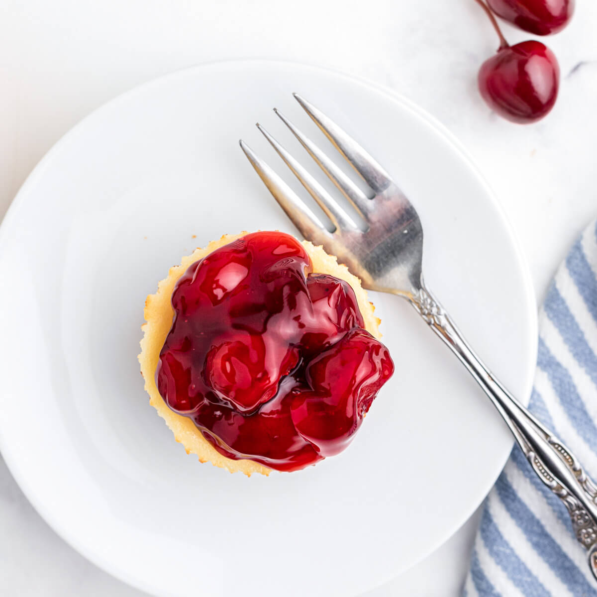 One mini cherry cheesecake with vibrant cherry topping on a white plate with a fork.