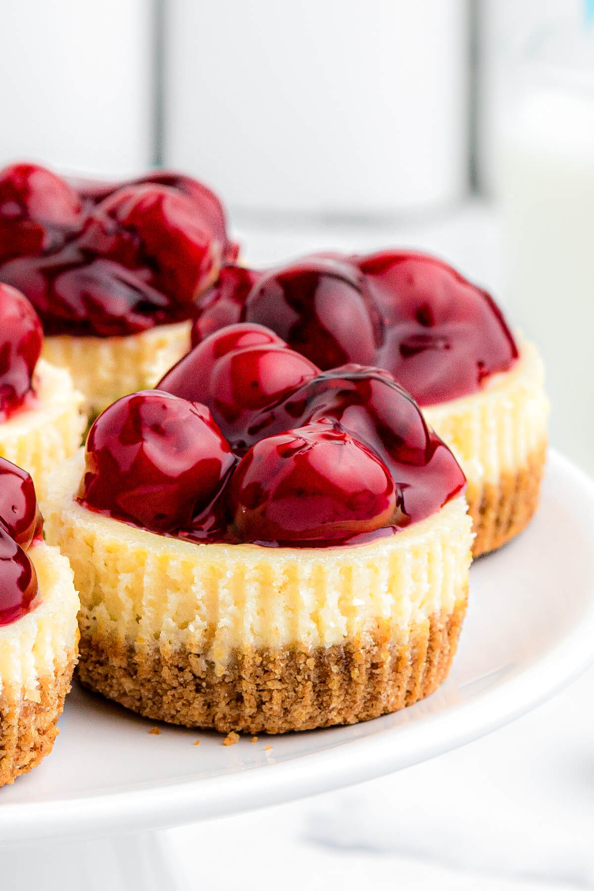 A group of Mini Cherry Cheesecakes showing the base graham crumb layer, middle cheesecake layer and glossy cherry pie filling topping.