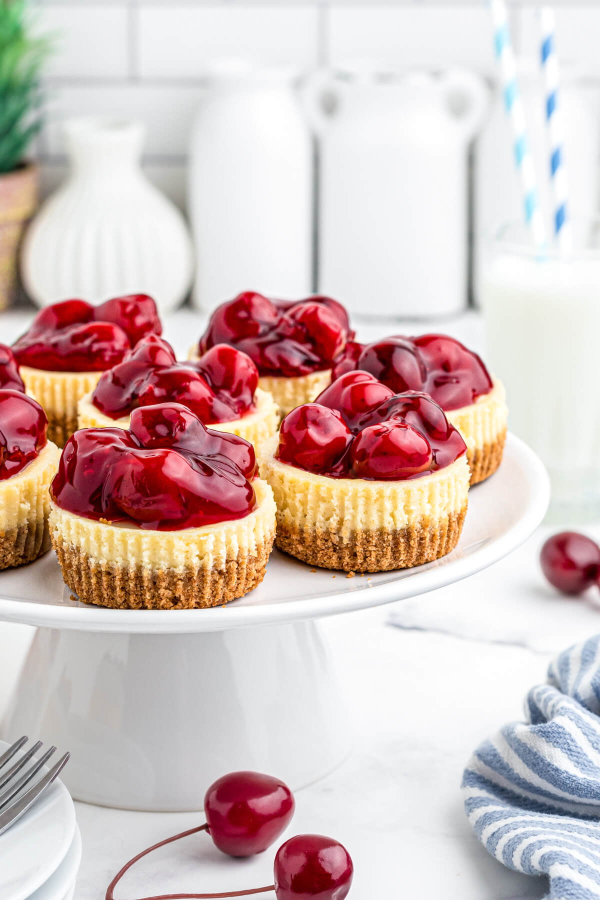 A group of Mini Cherry Cheesecakes on a white platter surrounded by fresh cherries.