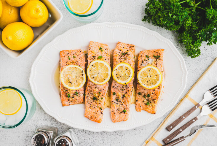 A white platter containing four oven baked lemon pepper salmon filets topped with lemon slices.