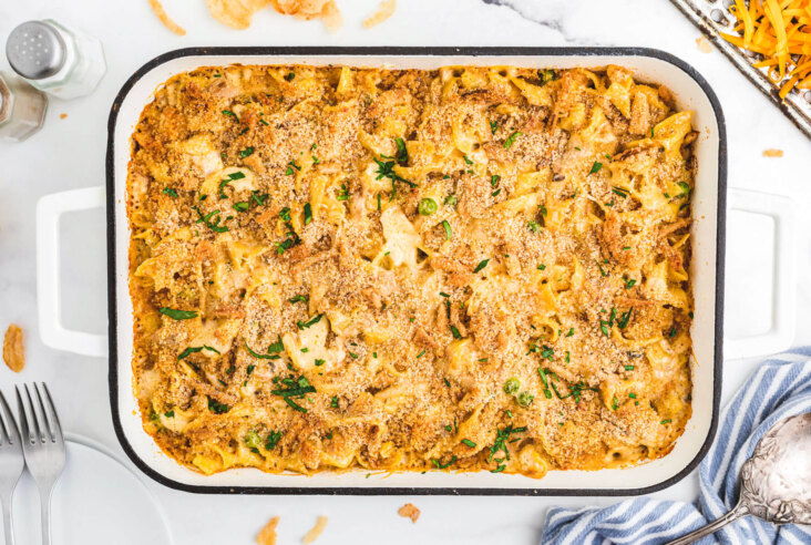 A white enamel baking pan full of golden baked, crumb topped Tuna Noodle Casserole.
