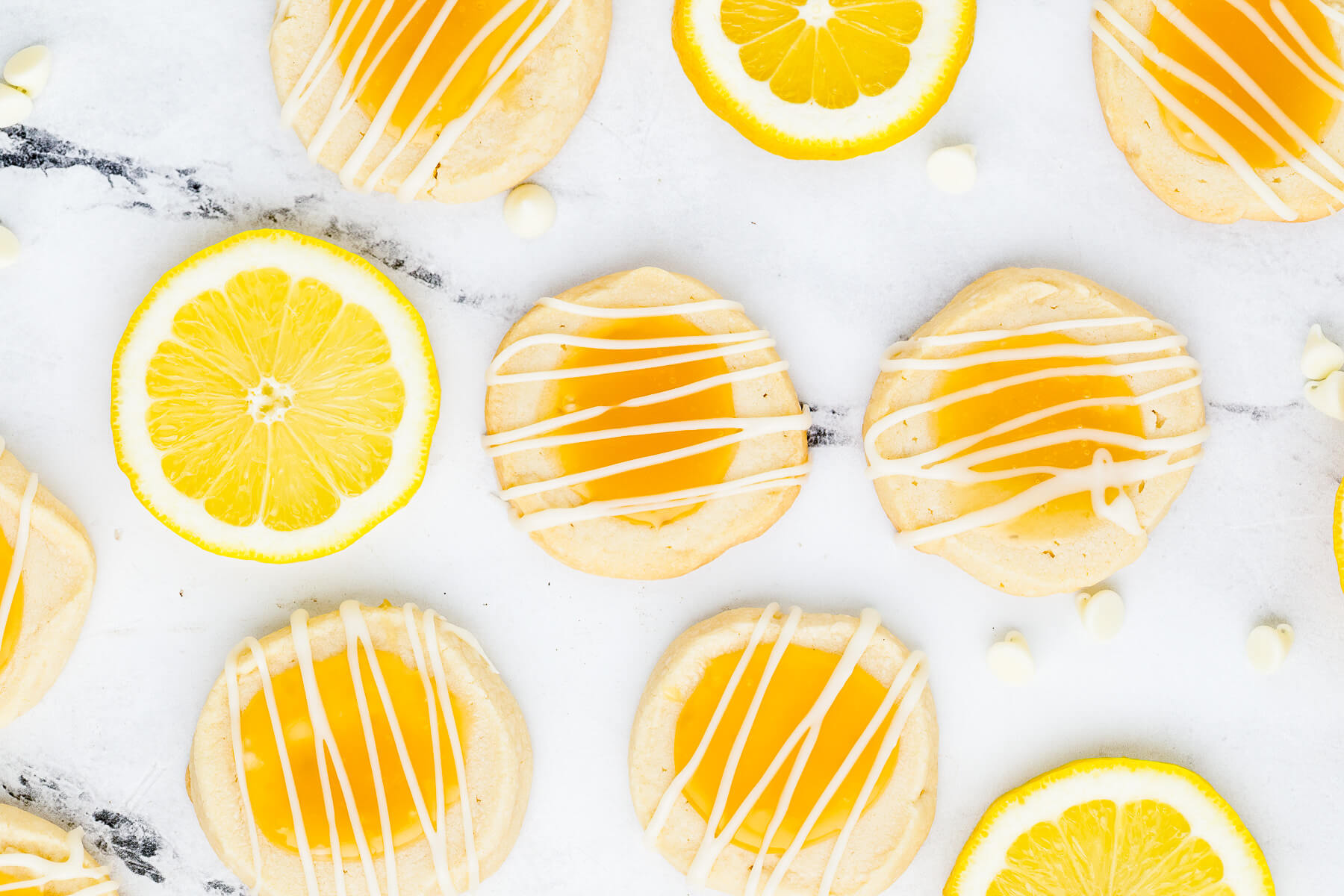 A group of Lemon curd thumbprint cookies topped with a white chocolate drizzle on white marble.