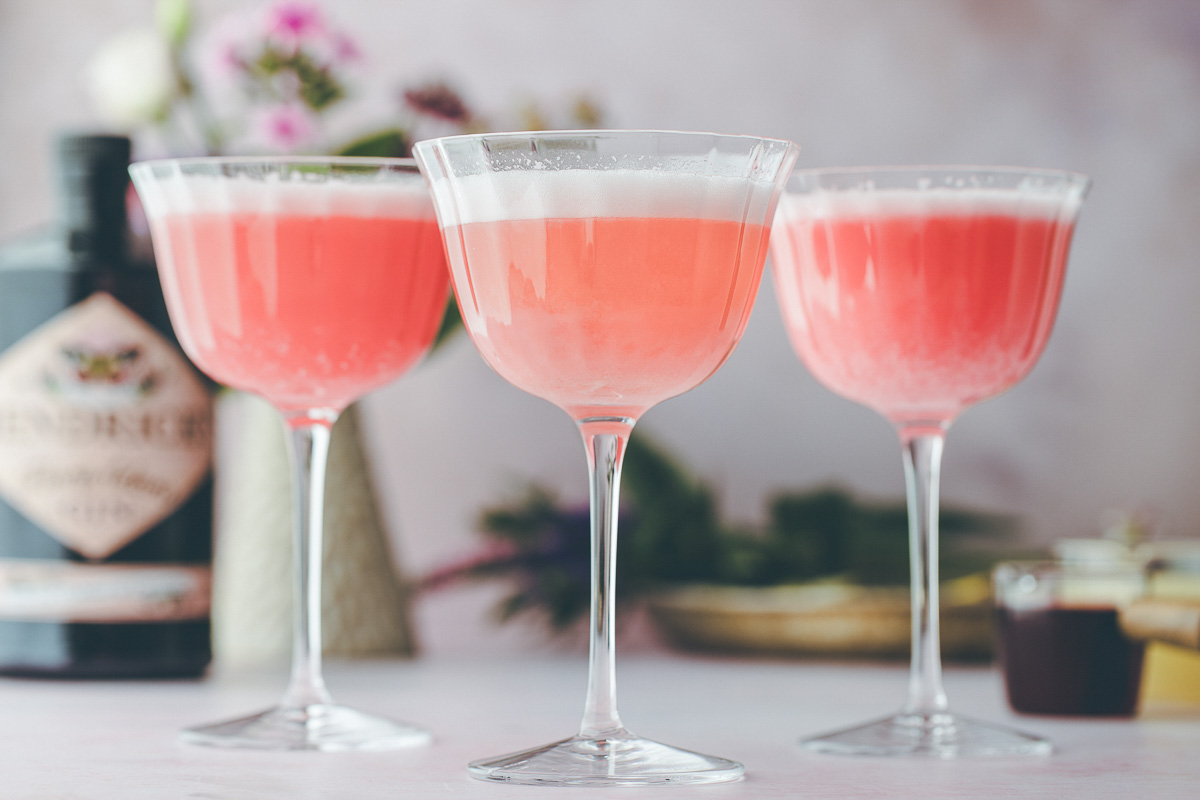 Three foam topped pink lady cocktails in coupe glasses.