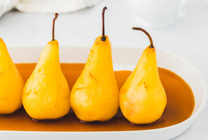 Three perfectly poached pears on a plate surrounded by sauce.