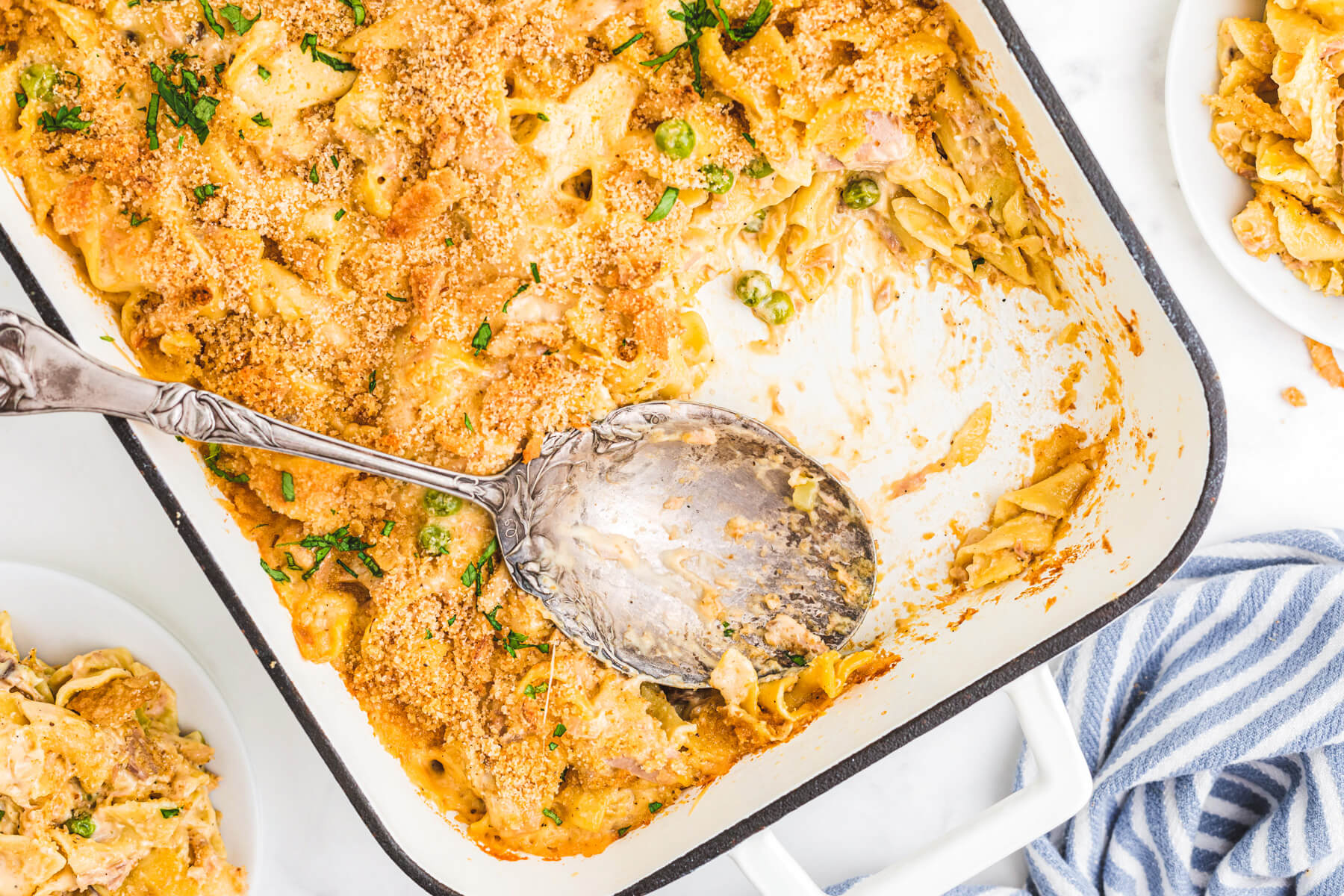 A white enamel baking pan half full of golden baked, crumb topped Tuna Noodle Casserole.