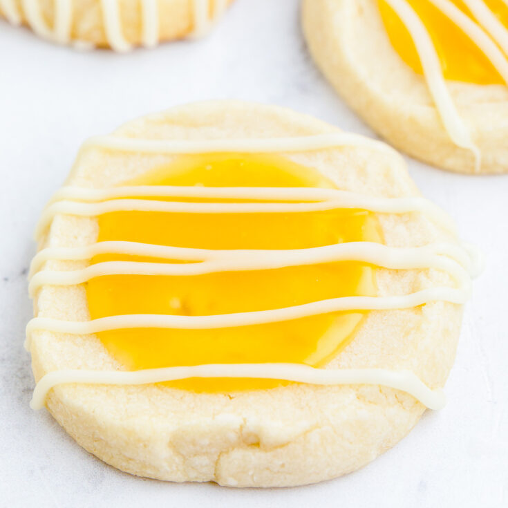 Three Lemon curd thumbprint cookies topped with a white chocolate drizzle.