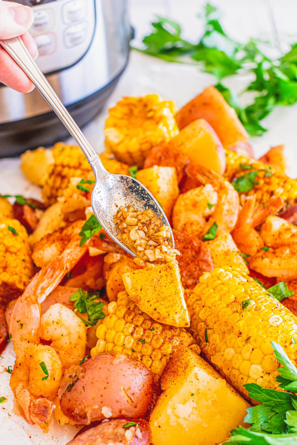 A hand spooning garlic sauce over a platter of low country shrimp boil.