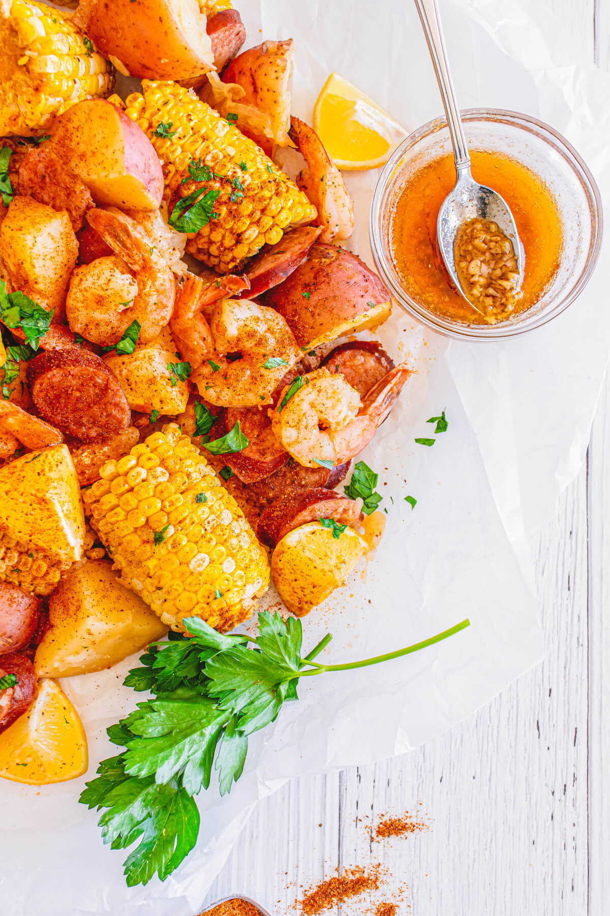 Cooked shrimp boil with spice coated shrimp, potatoes, sausage, and corn spread out on a white parchment paper.
