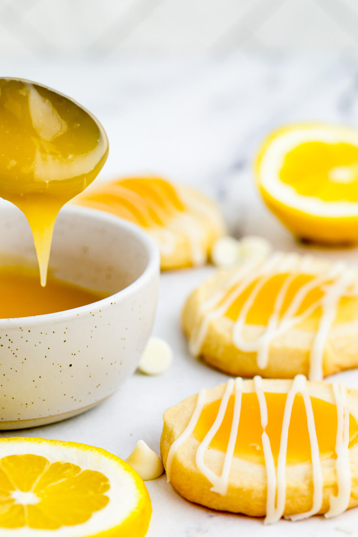 A spoon drizzles lemon curd over a small bowl sitting beside several lemon curd cookies.