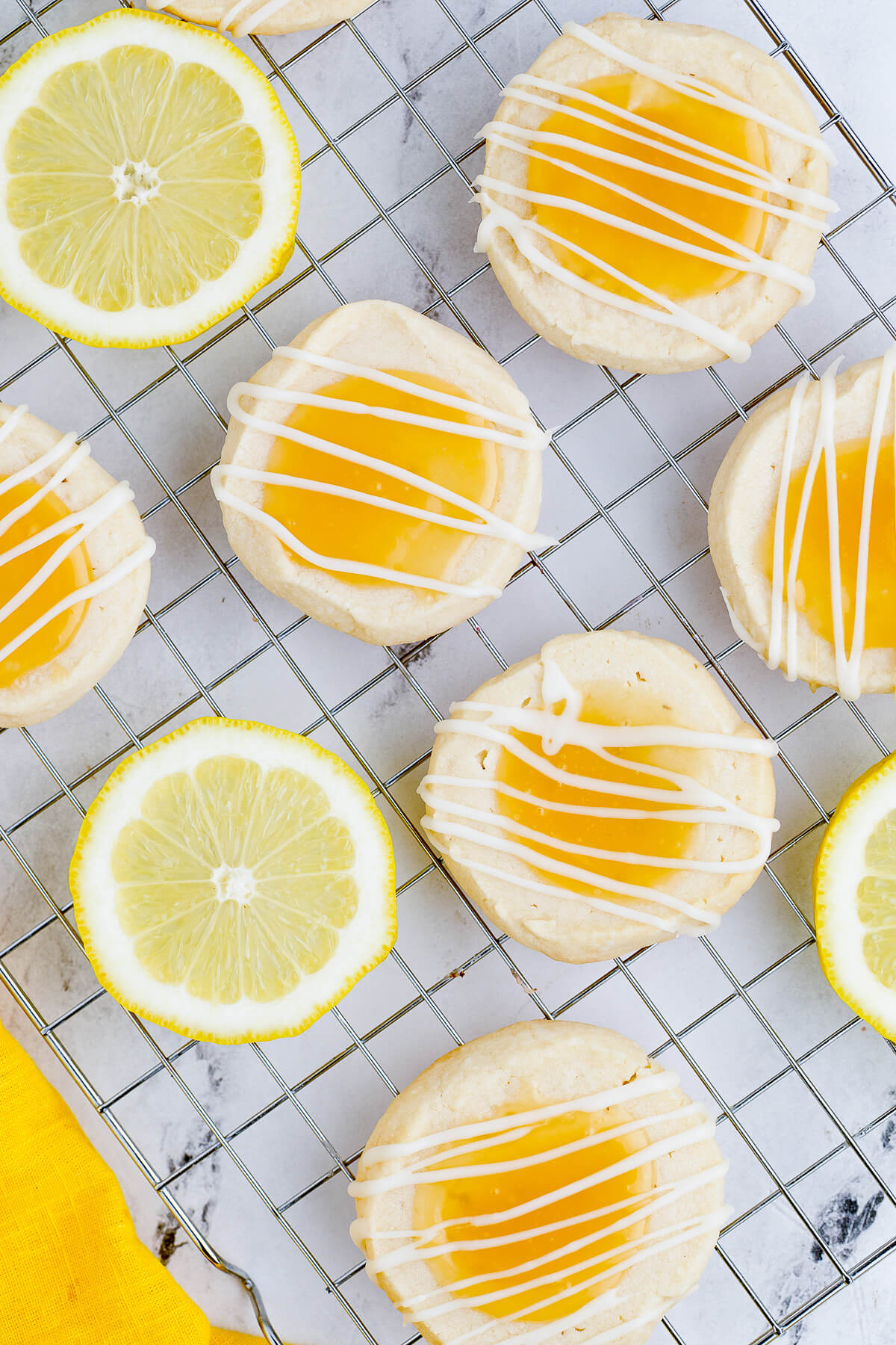 A group of Lemon curd thumbprint cookies topped with a white chocolate drizzle on a cooling rack.