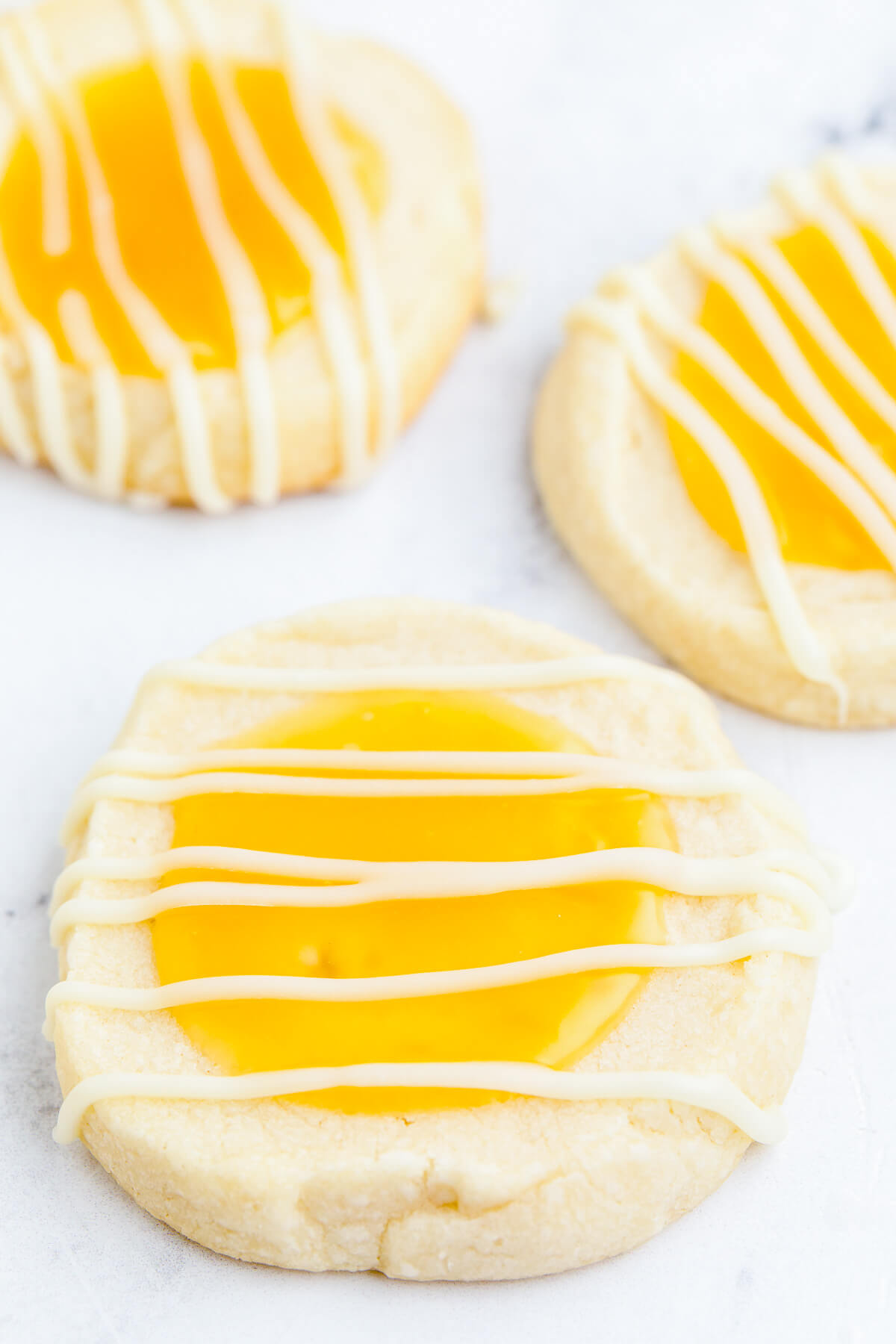 Three Lemon curd thumbprint cookies topped with a white chocolate drizzle.