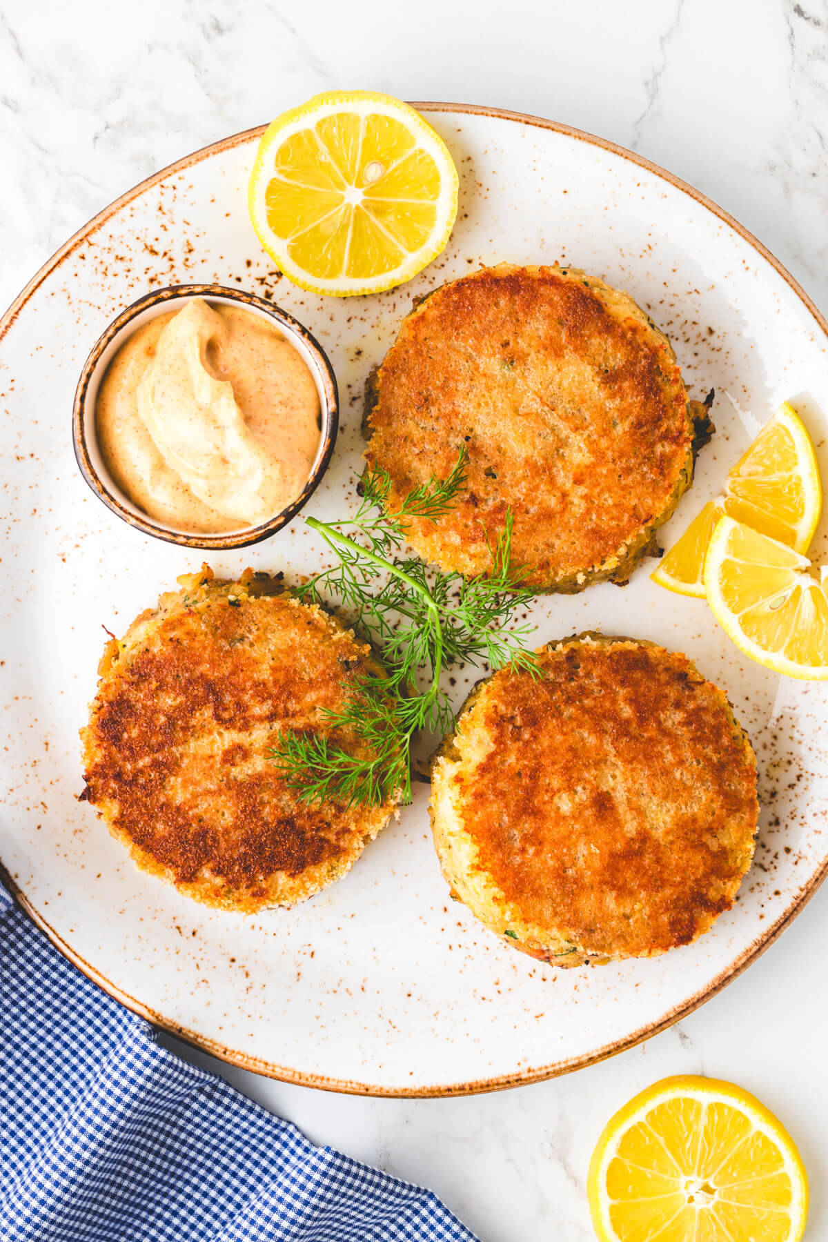A white plate featuring three old bay seasoned crab cakes, lemon slices, and Cajon aioli.