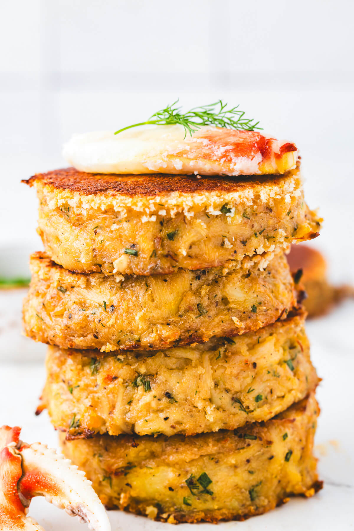 A stack of golden fried crab cakes topped with a dollop of Cajun aioli and fresh dill garnish.