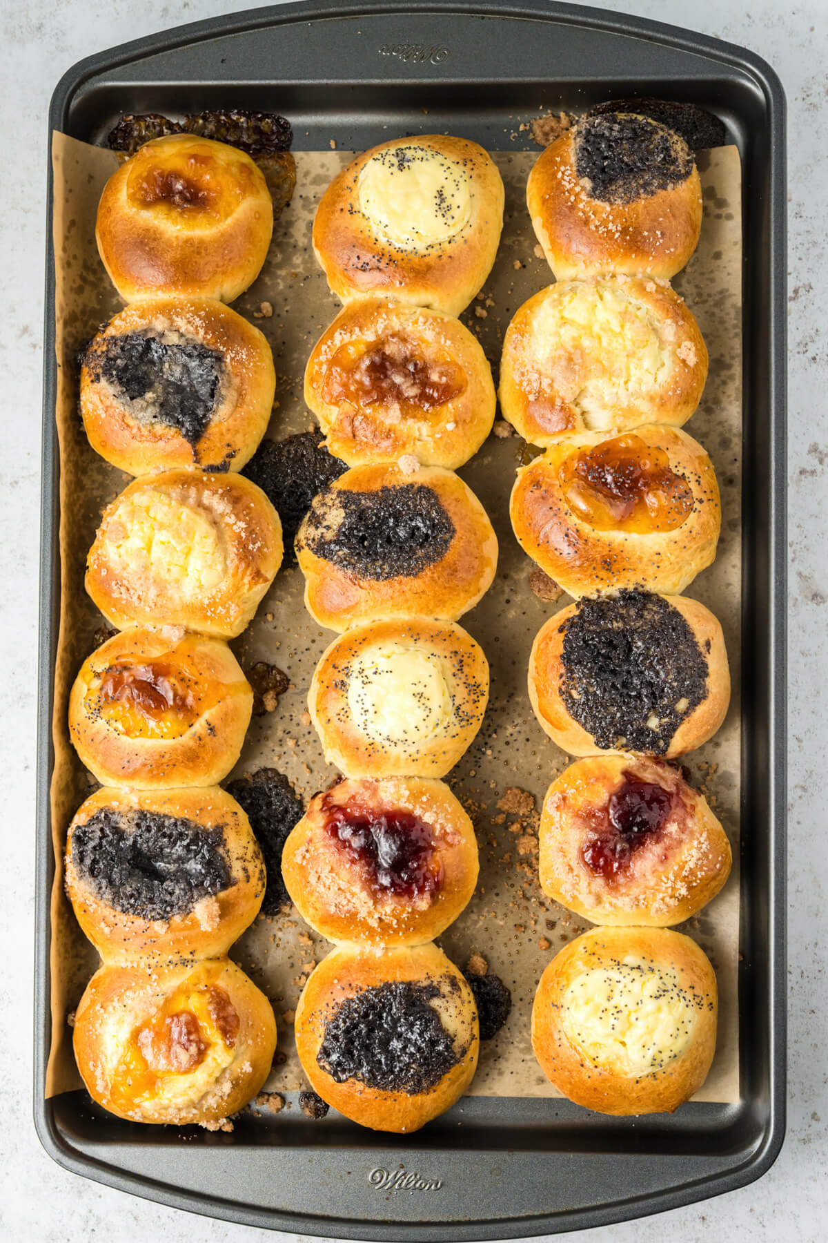 A baking sheet full of golden baked kolaches filled with a variety of fillings. 