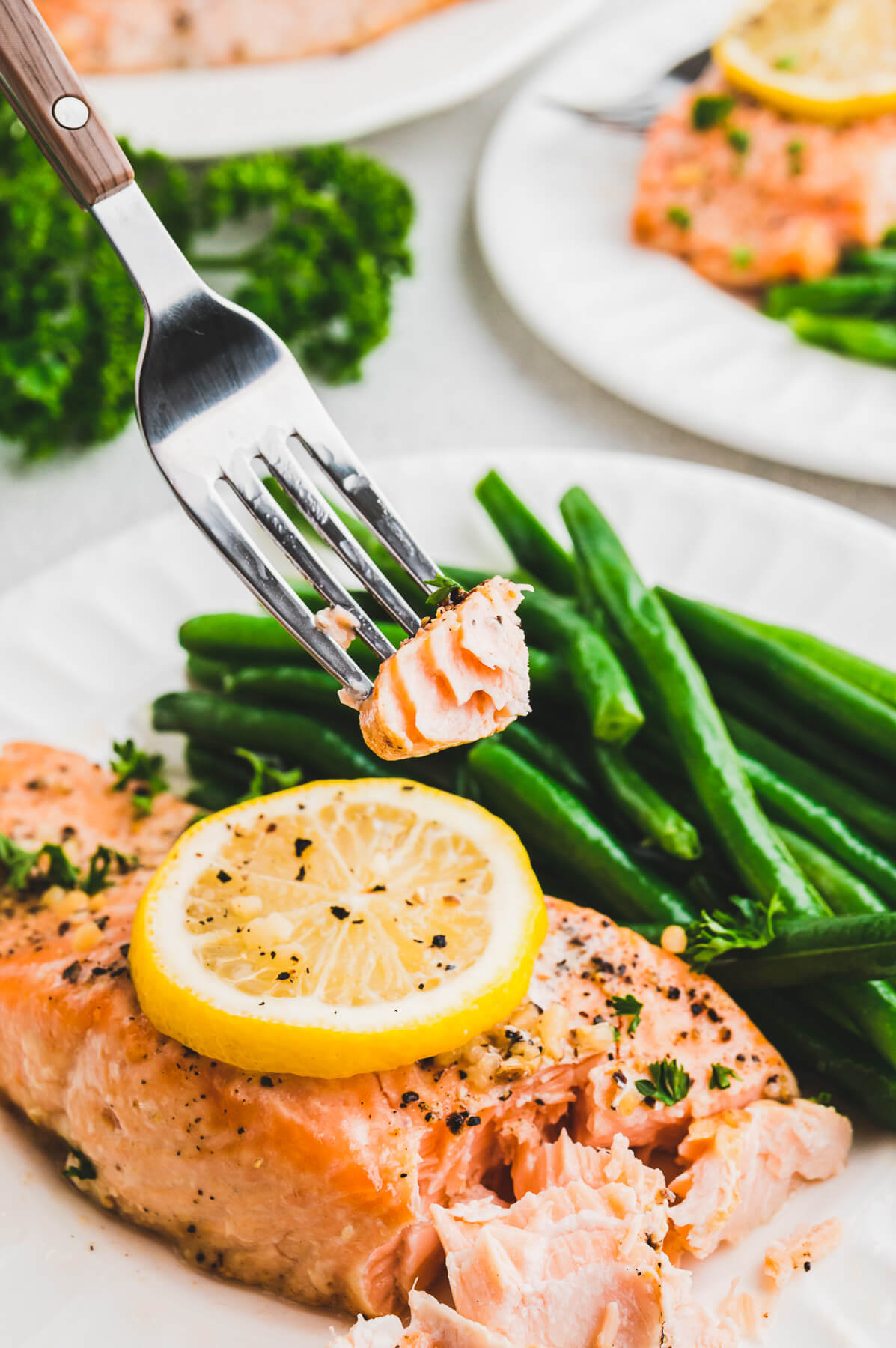 A fork holding a bite of salmon over a full white dinner plate of salmon and beans.
