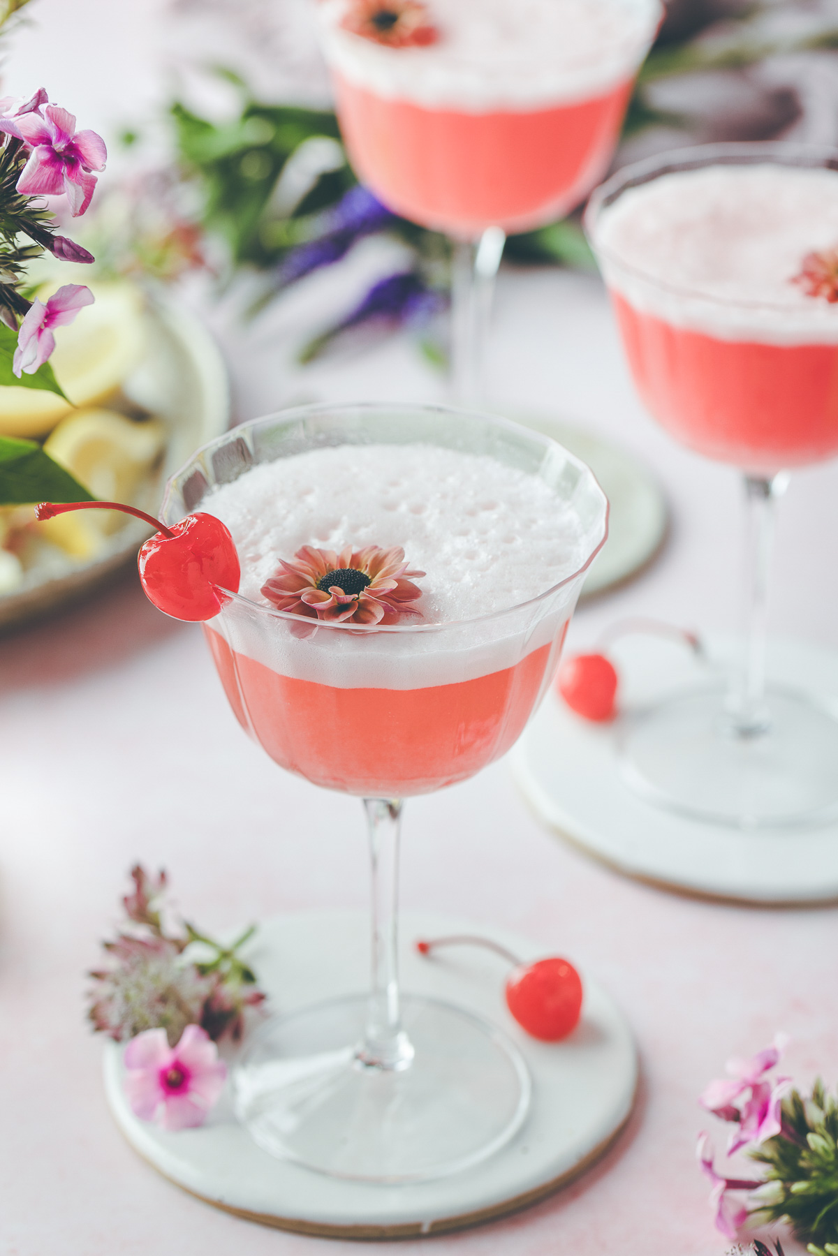 Three lovely pink lady cocktails garnished with bright red cherries and edible flowers. 
