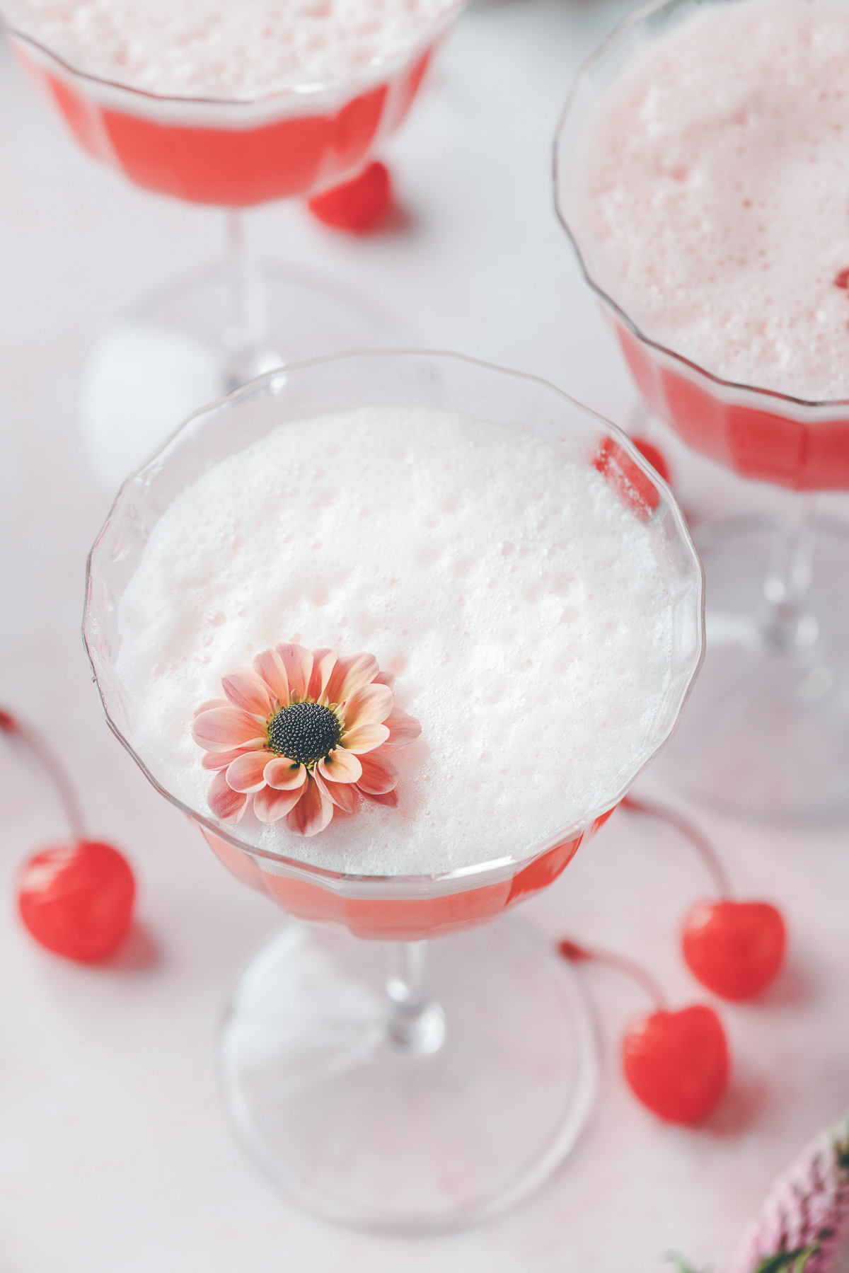 One pink lady cocktail garnished with a bright red cherry and an edible flower.