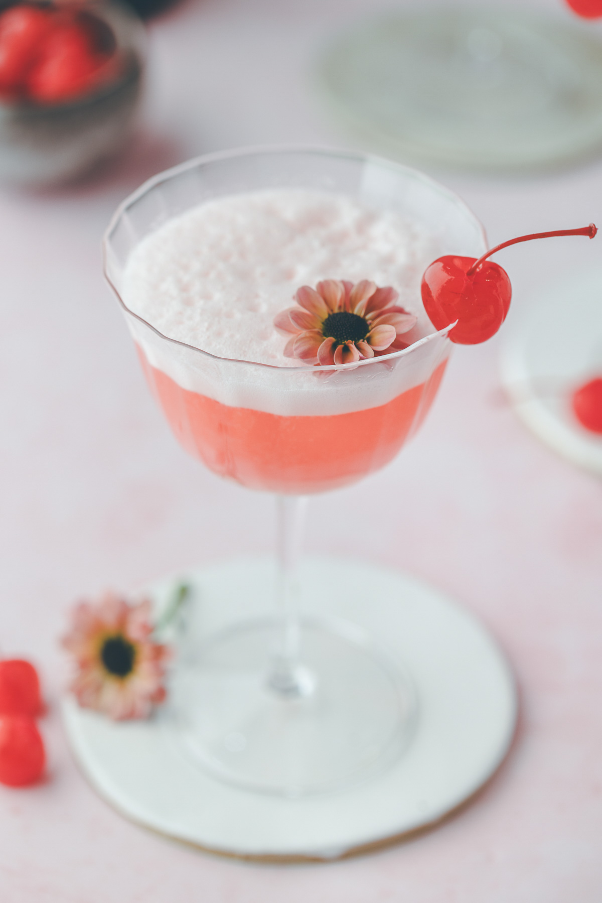 One pink lady cocktail garnished with a bright red cherry and an edible flower.